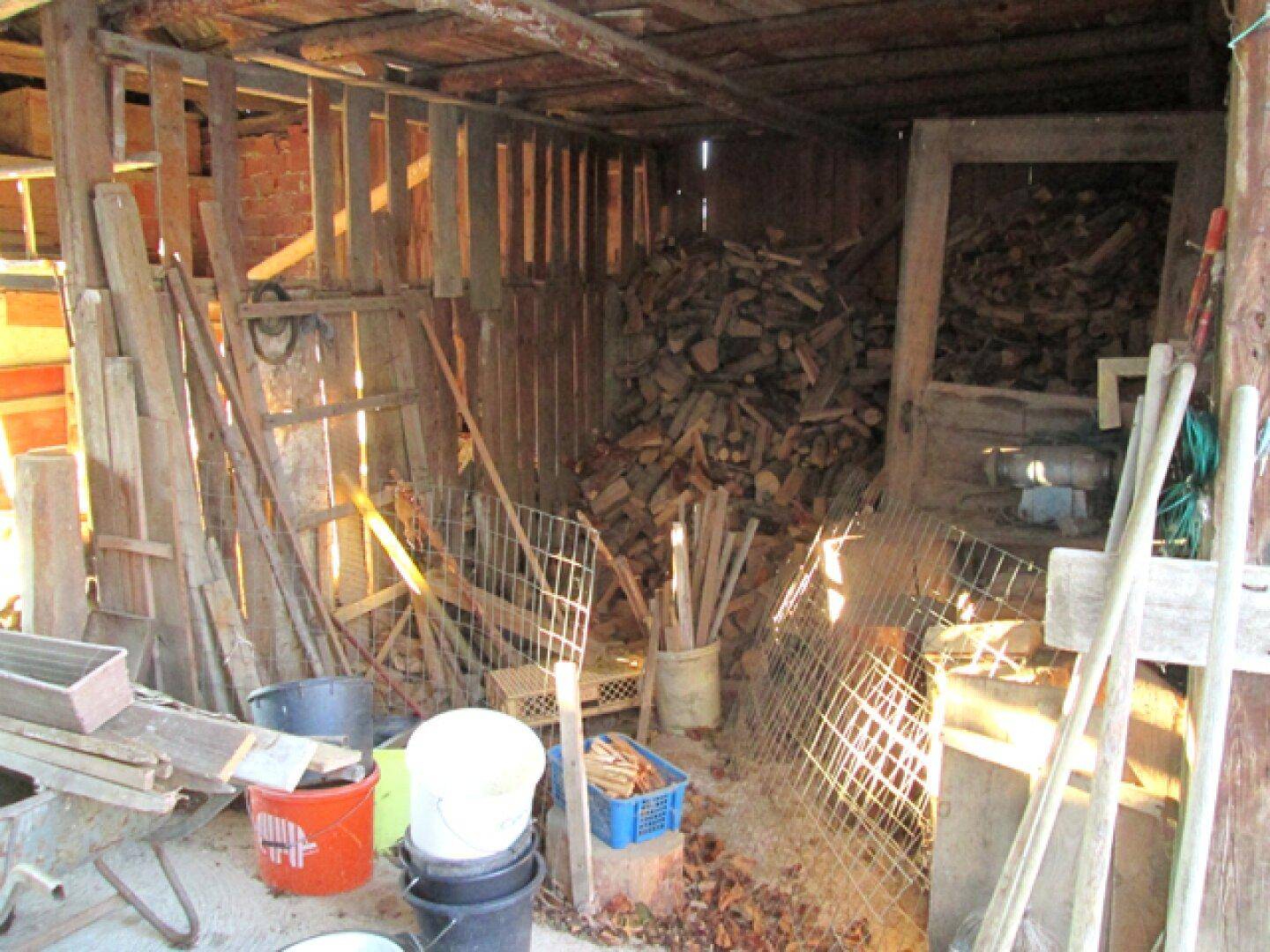 Innenansicht einer Scheune mit einem großen Stapel Brennholz und verschiedenen Geräten.