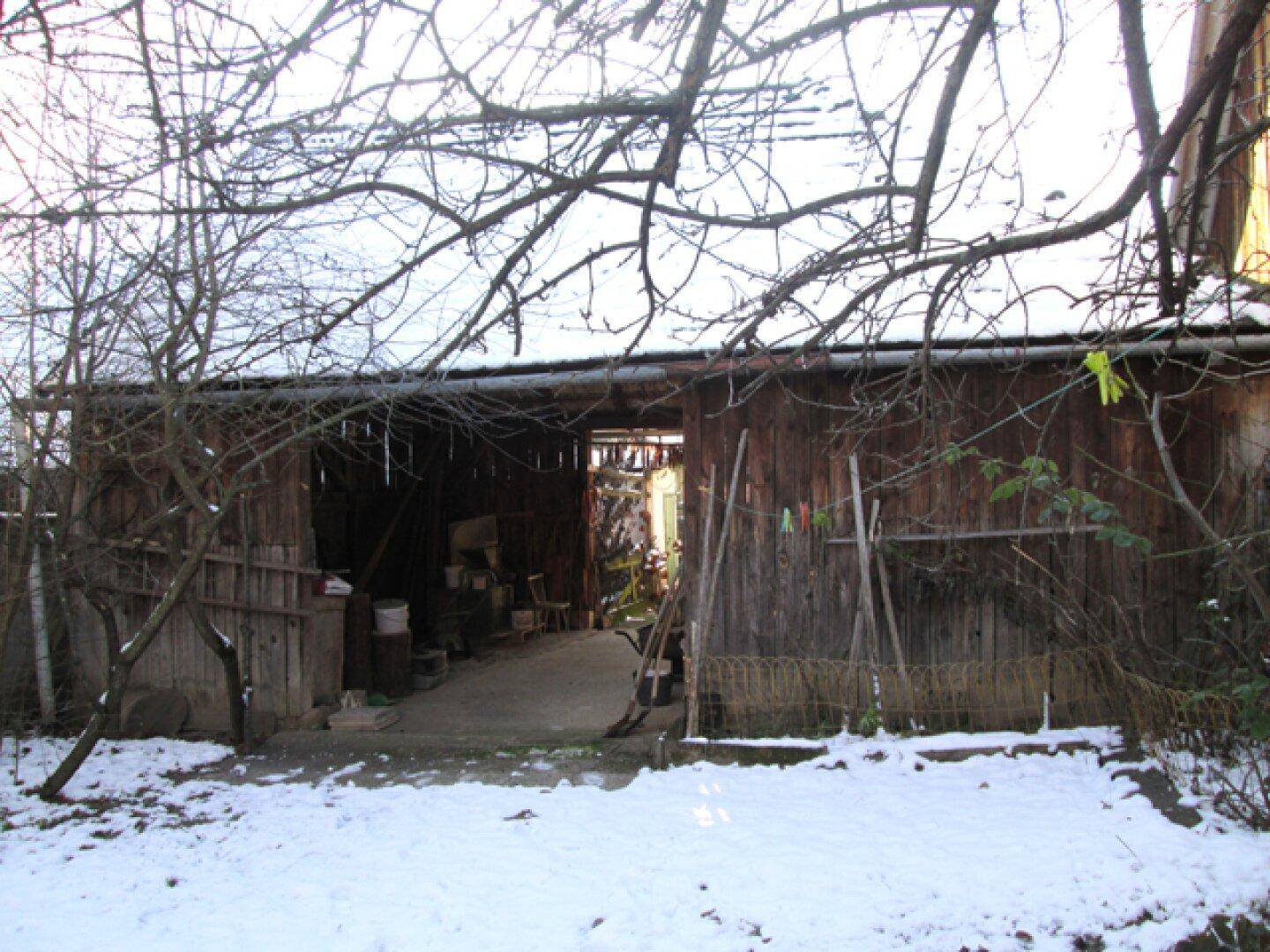 Außenansicht einer Scheune mit Holzwänden und einem schneebedeckten Vorplatz.