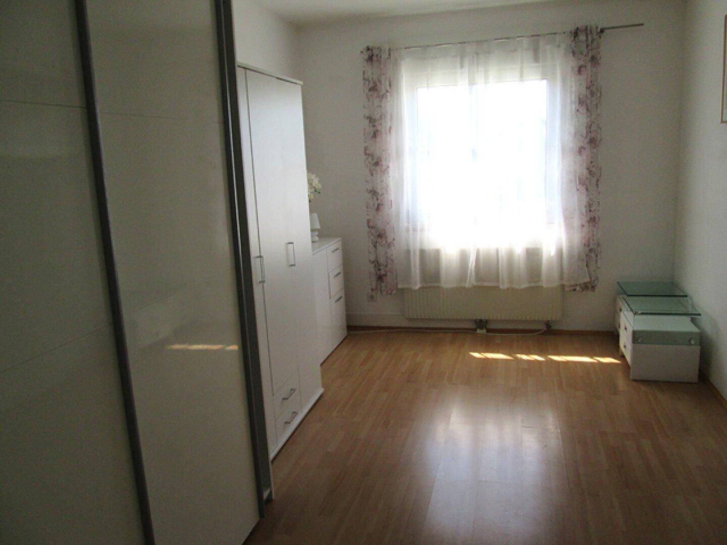 Helles Schlafzimmer mit Parkettboden, weißen Schränken und großem Fenster.