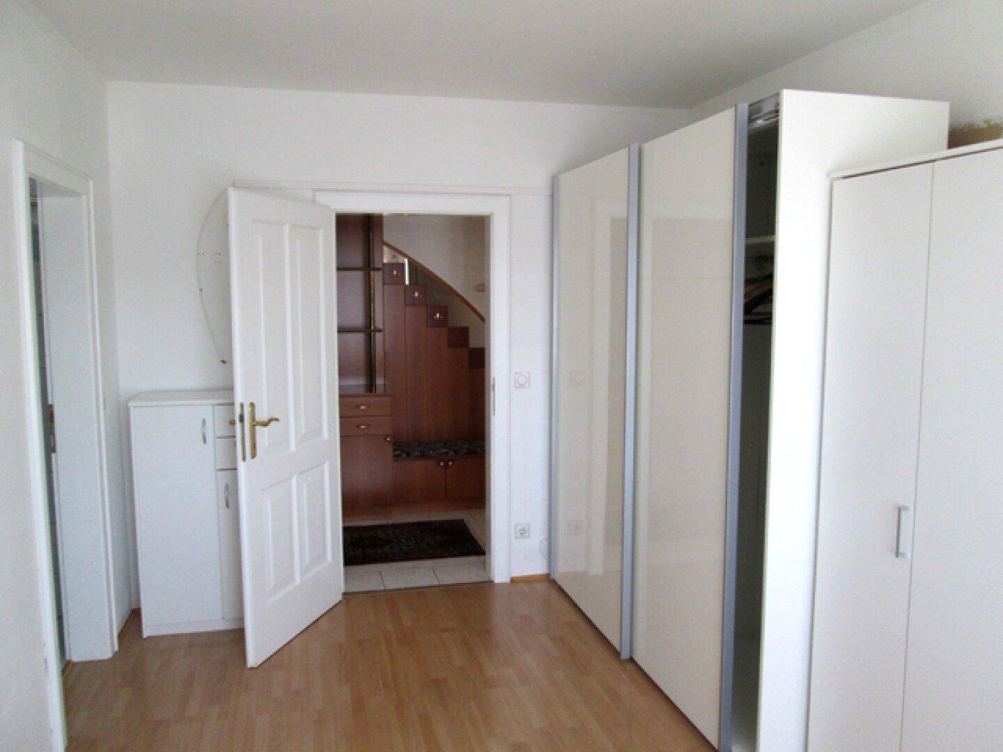 Schlafzimmer mit Parkettboden, weißen Schränken und Zugang zum Flur.