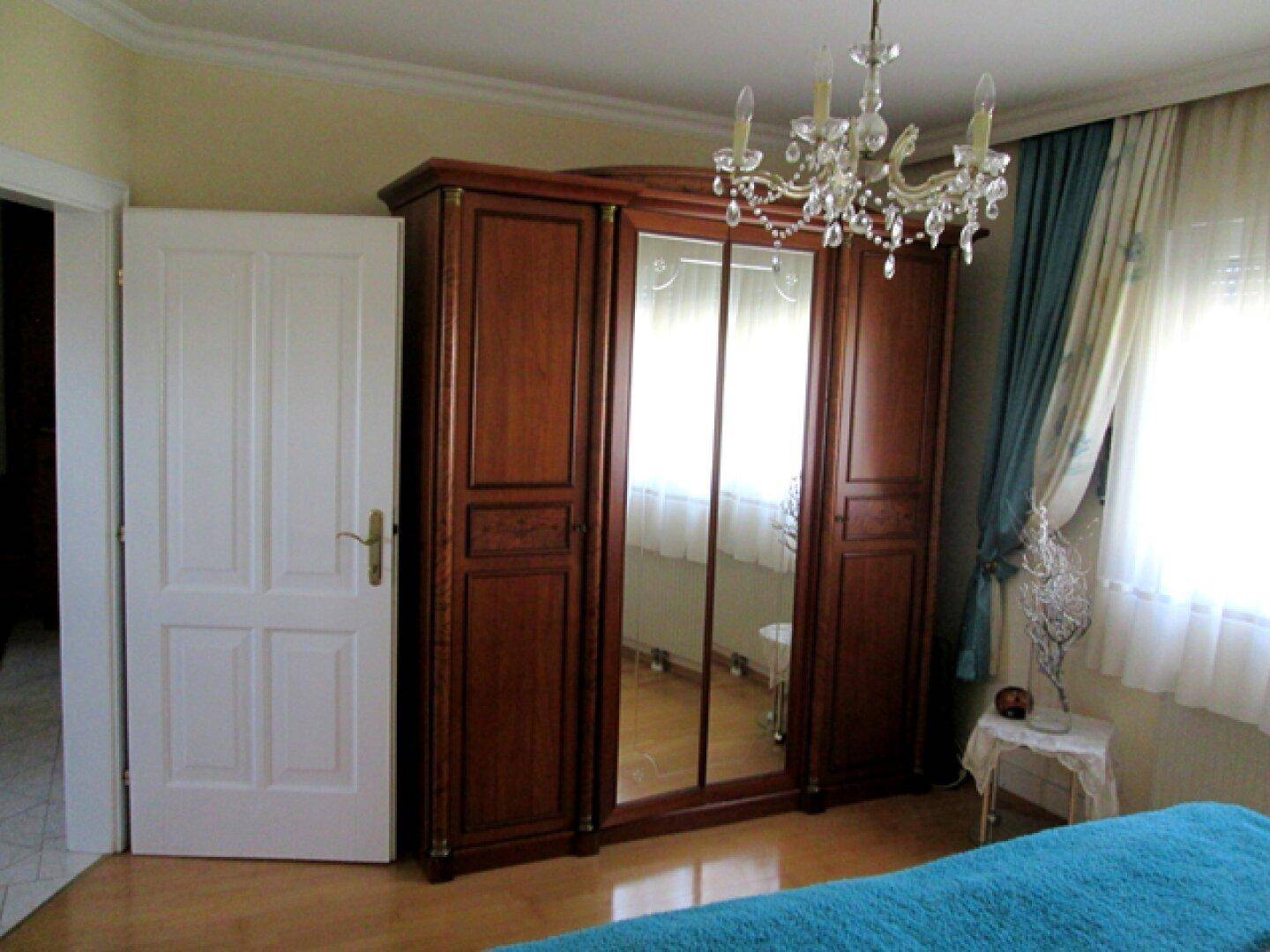 Schlafzimmer mit einem großen, klassischen Holzschrank mit Spiegeltüren und Holzboden.