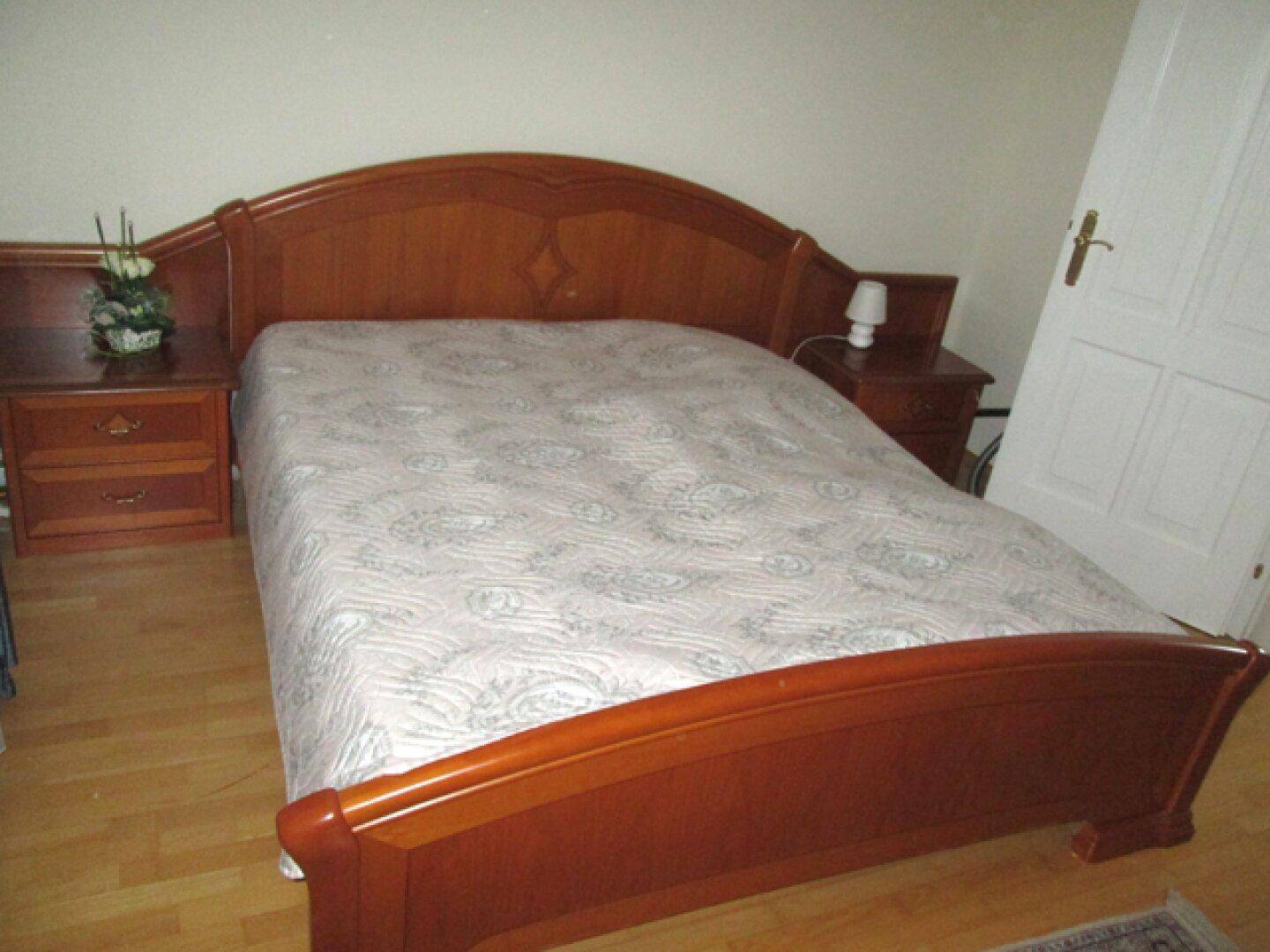 Schlafzimmer mit einem klassischen Holzbettrahmen und passenden Nachttischen auf Parkettboden.