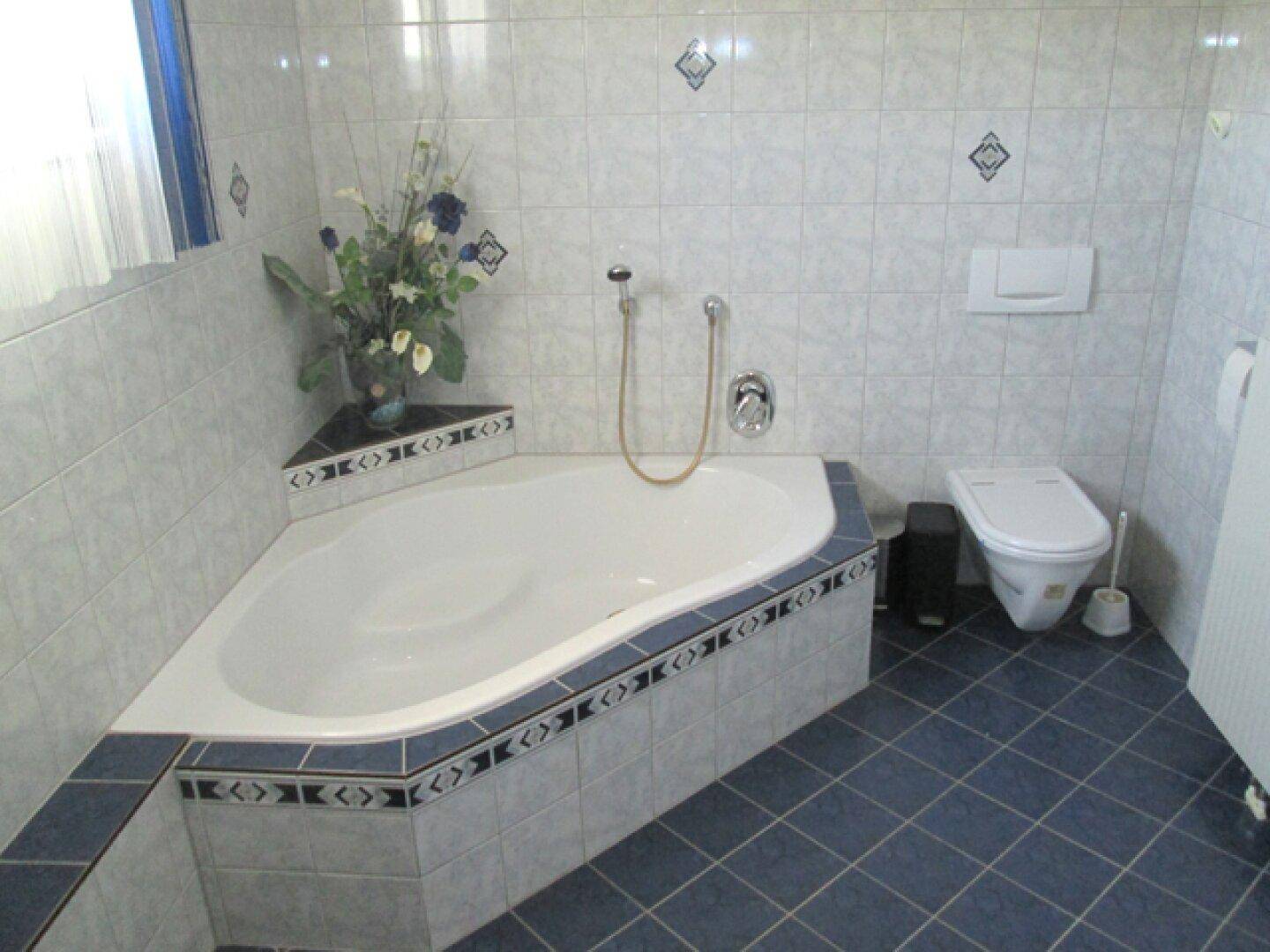 Badezimmer mit einer Eckbadewanne und Toilette, gefliest in einem Muster aus Blau und Weiß.