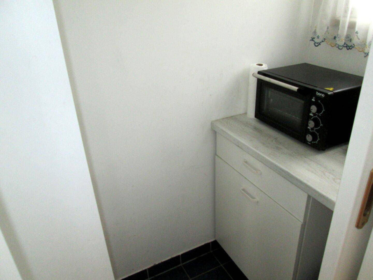 Kompakte Speisekammer mit Arbeitsplatte, kleinem Ofen und dunklem Fliesenboden.