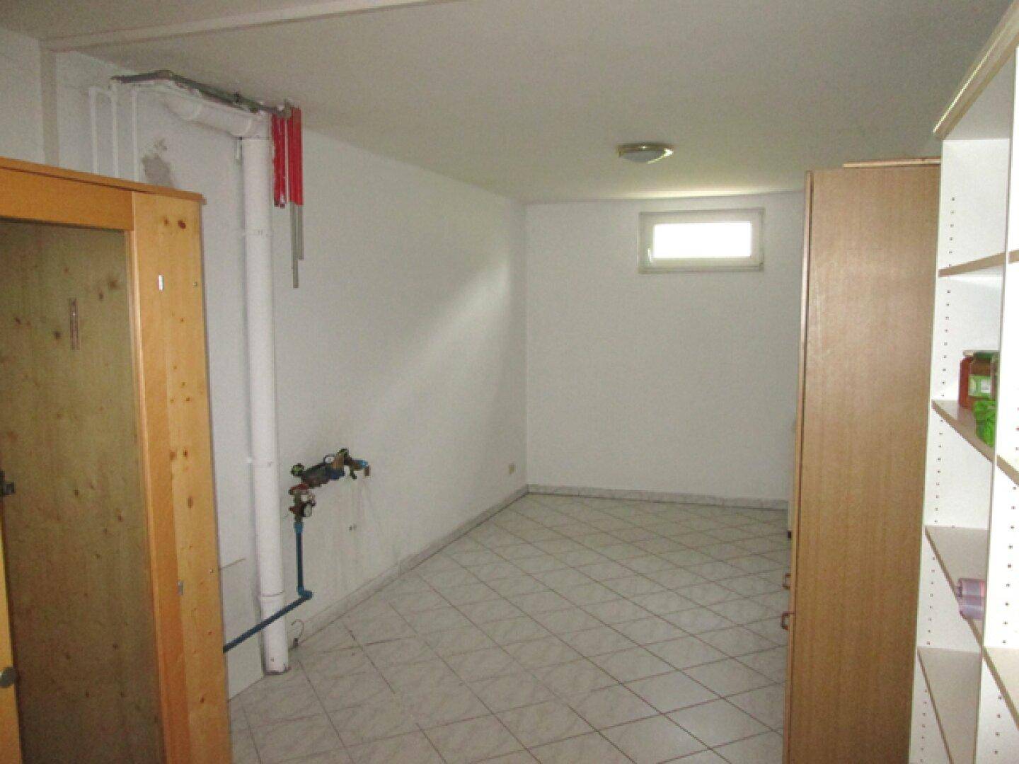 Kellerraum mit Fliesenboden, kleinem Fenster und sichtbaren Leitungen, als Abstellraum nutzbar.