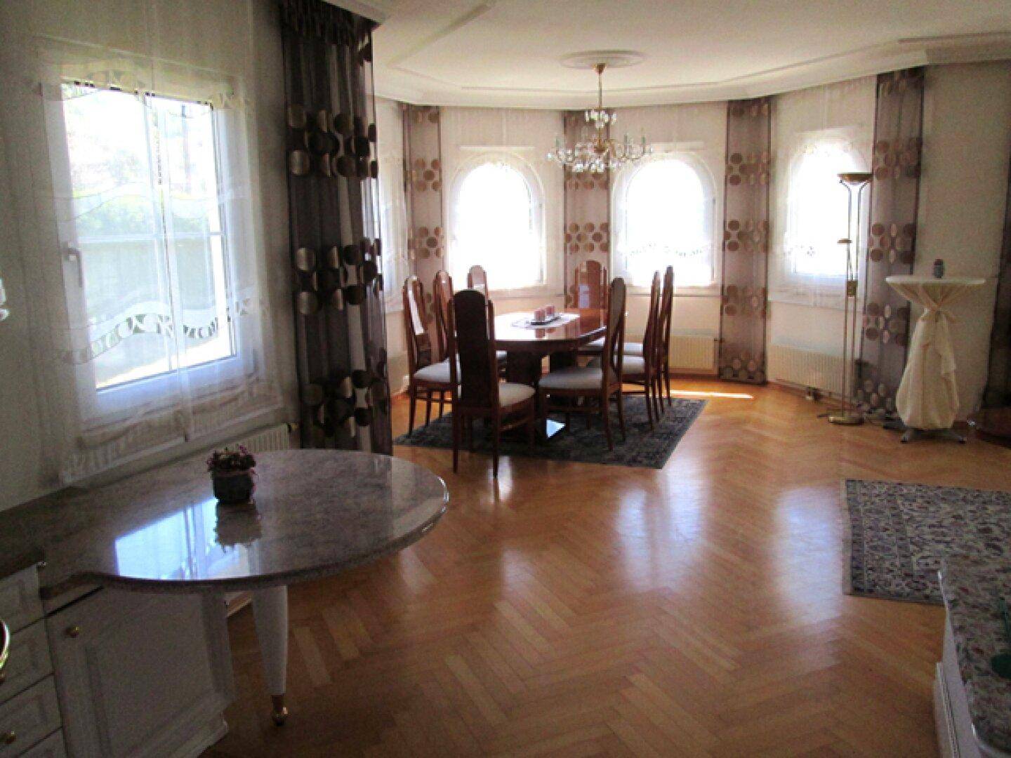 Heller Essbereich mit großem Holztisch, Stühlen und Rundbogenfenstern, die viel Tageslicht hereinlassen.