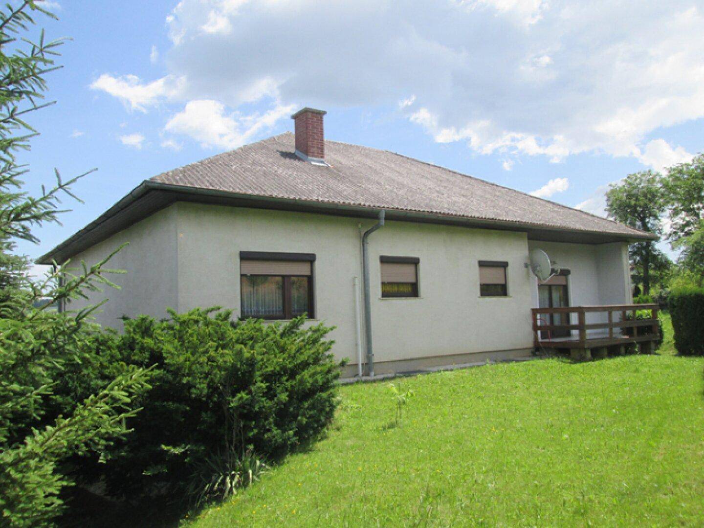 Rückseite des Hauses mit Rasenfläche und kleiner Holzterrasse unter einem hellen Himmel.