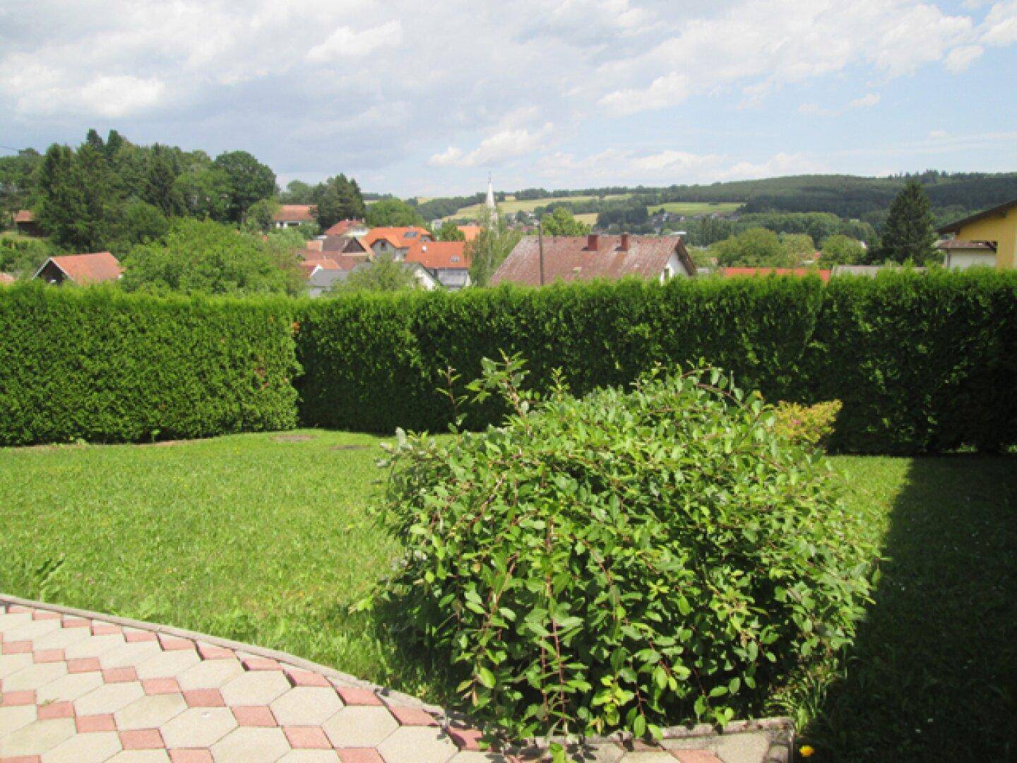 Garten mit Blick auf die umliegende Landschaft und eine Siedlung im Hintergrund an einem sonnigen Tag.