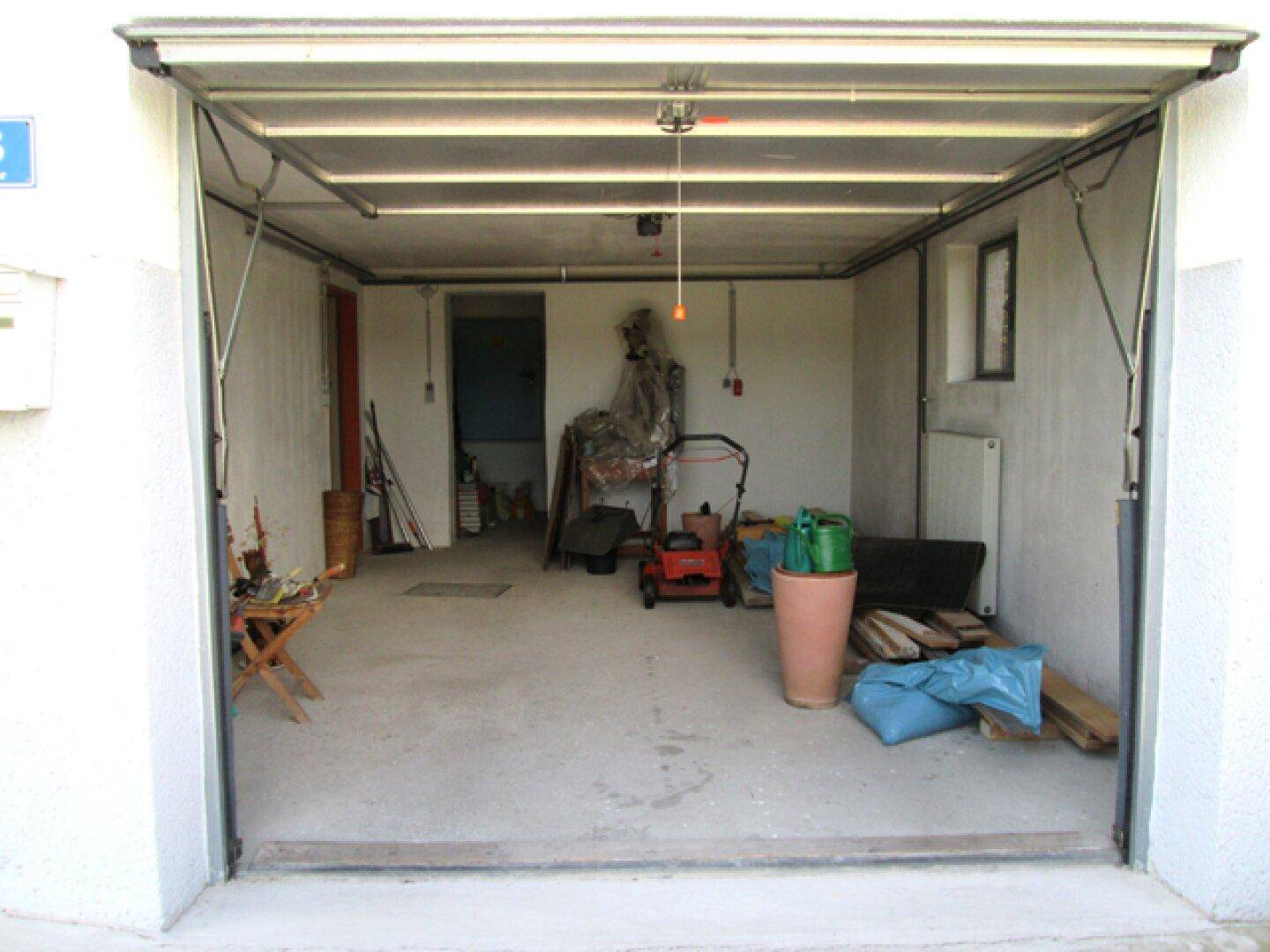 Offene Garage mit Betonboden, verschiedenen Werkzeugen und Gartengeräten.