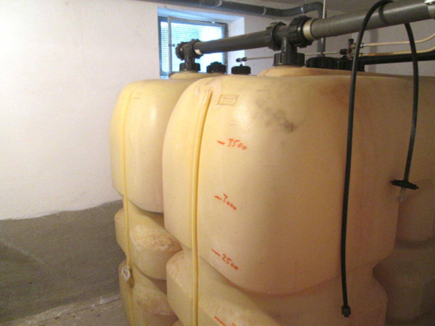 Kellerraum mit großen beigen Tanks, Rohrleitungen und einem kleinen Fenster.