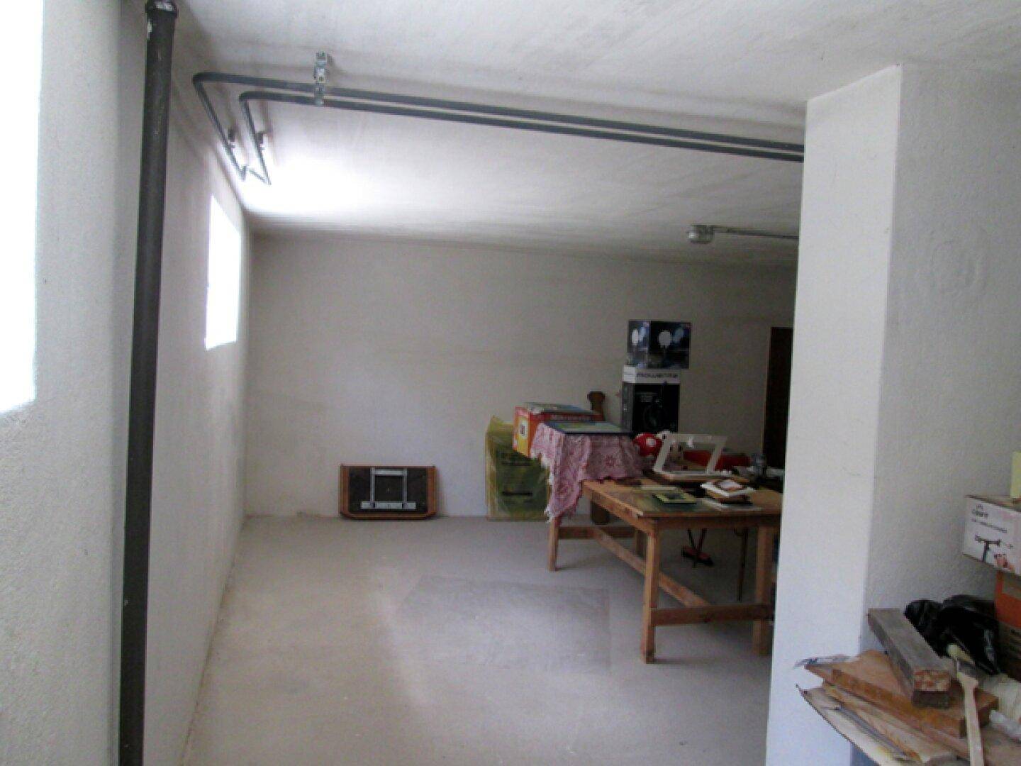 Langer, schmaler Kellerbereich mit Fenstern, sichtbaren Rohrleitungen und Betonboden.