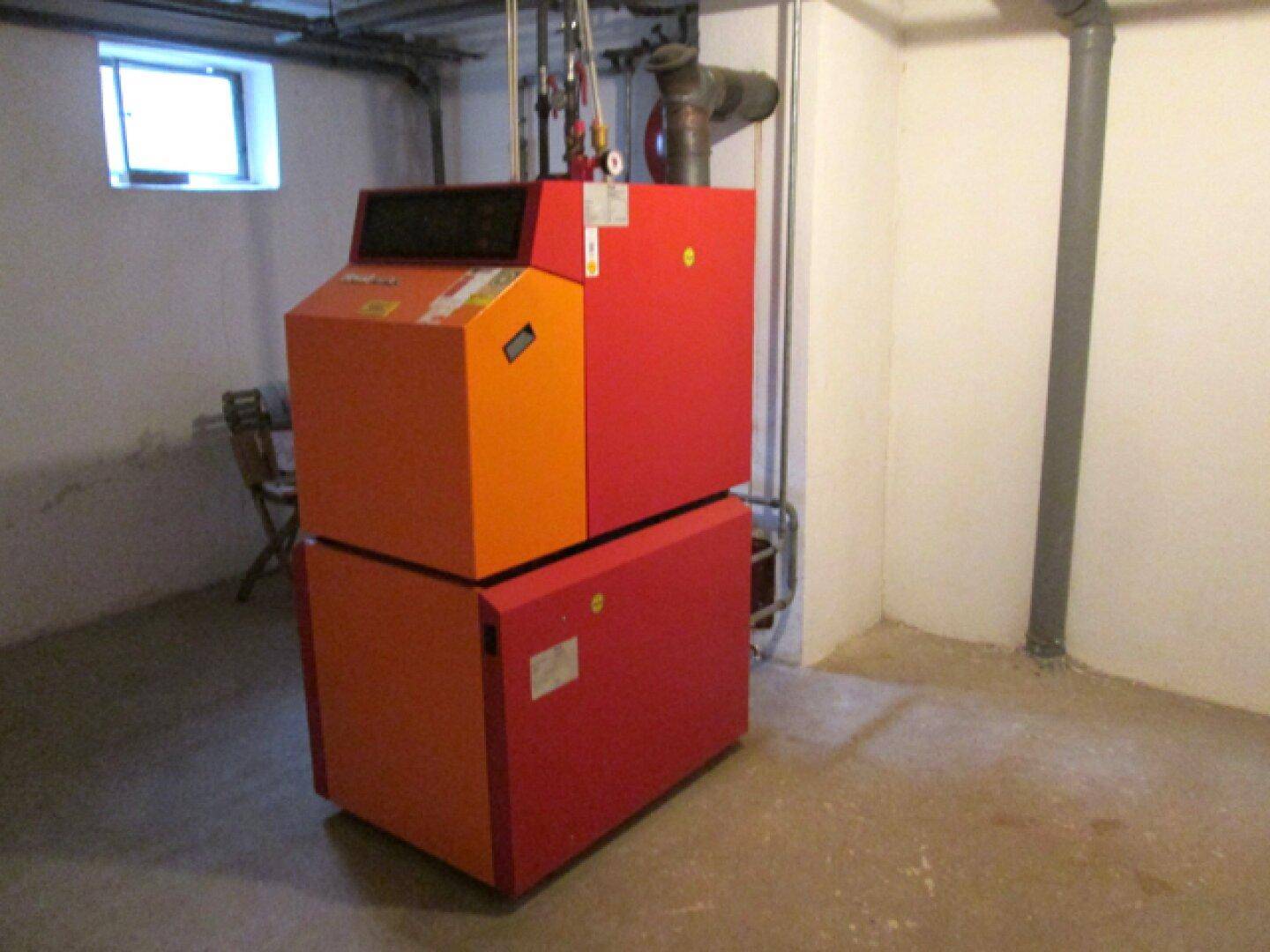 Heizungsanlage mit orange-rotem Kessel in einem sauberen Hauswirtschaftsraum.
