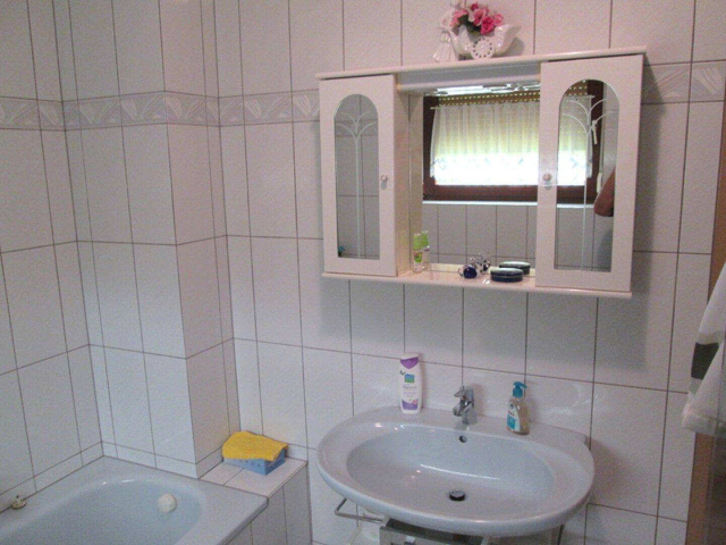 Badezimmer mit Waschbecken, Spiegelschrank und Fenster für natürliche Belüftung und Helligkeit.