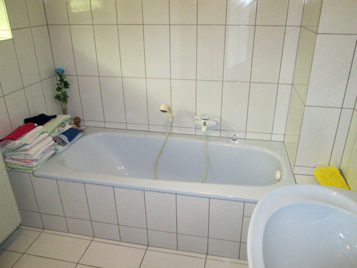 Badezimmer mit eingebauter Badewanne, weißen Fliesen und Ablagefläche für Handtücher.
