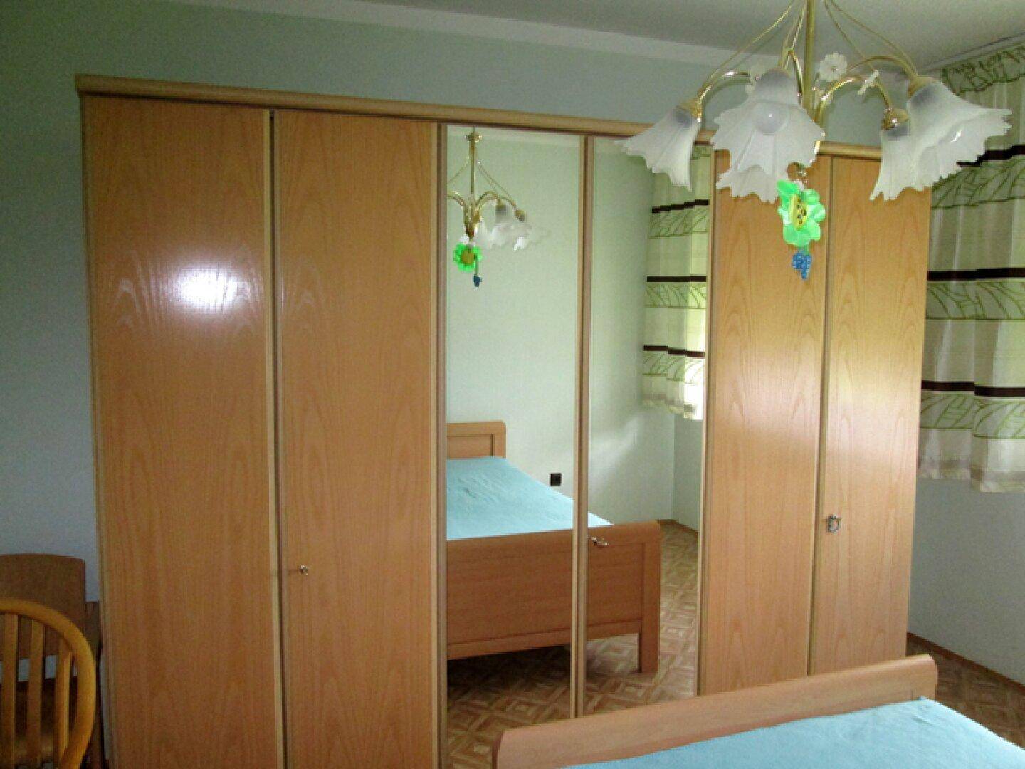 Schlafzimmer mit großem Holzschrank, Spiegeltüren und Blick auf das Bett und den Raum.