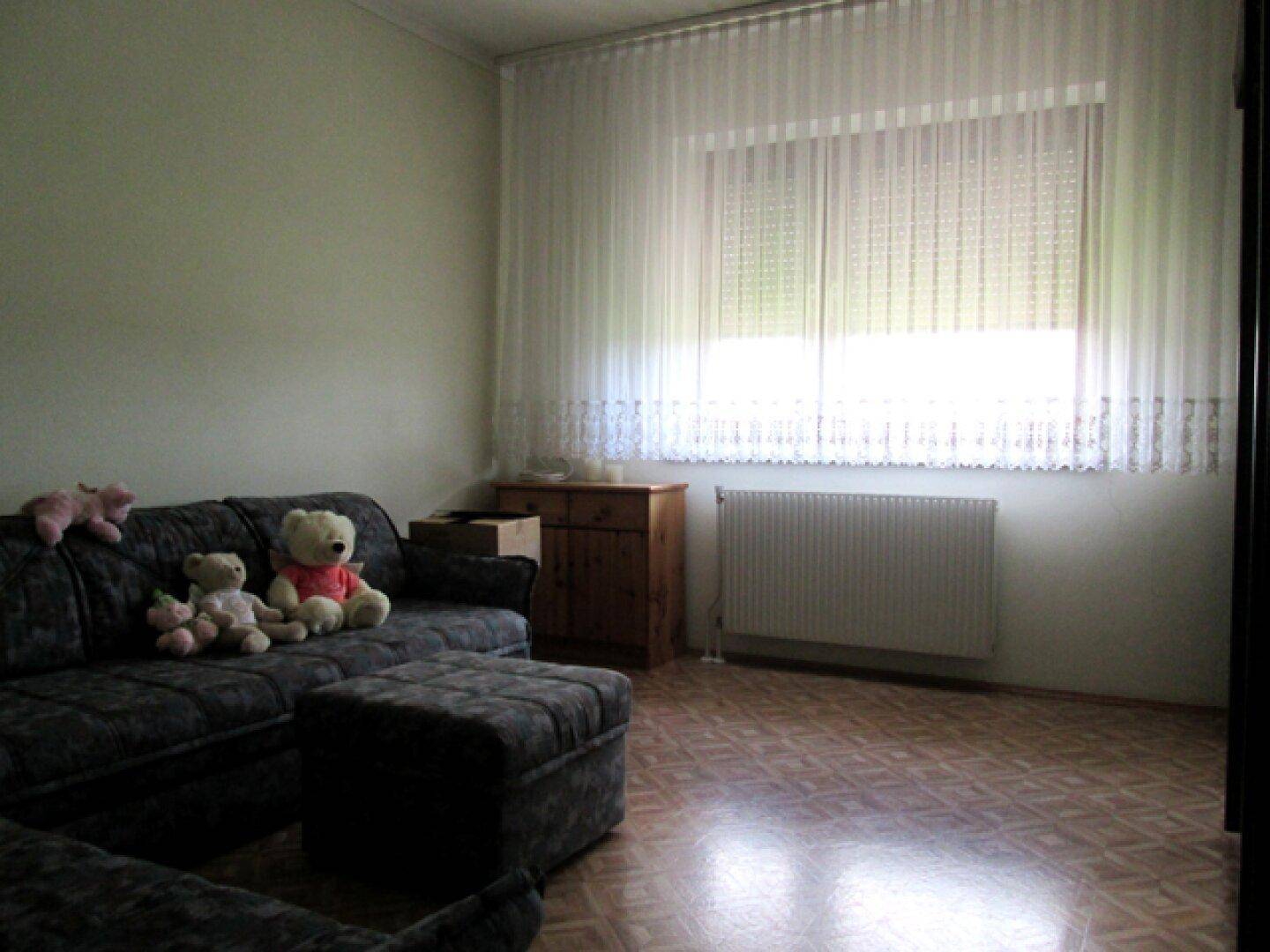 Wohnzimmer mit dunklem Sofa, Laminatboden und großem Fenster für Helligkeit und Ausblick.