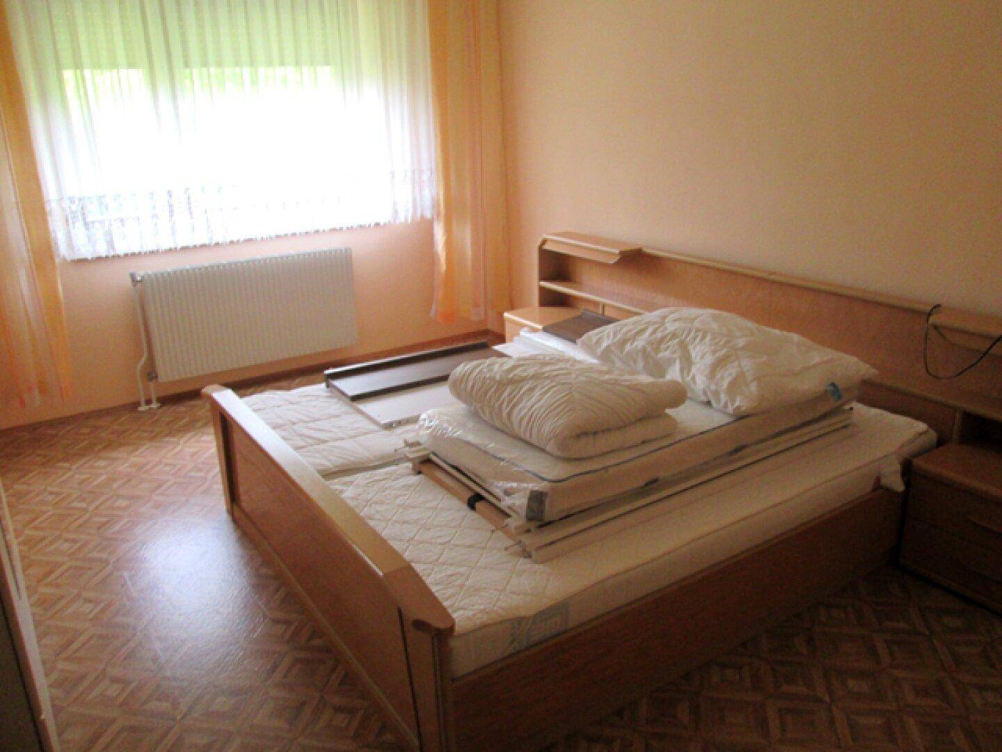 Schlafzimmer mit Holzbett, Nachttischen und Fenster mit hellem Vorhang für natürliches Licht.