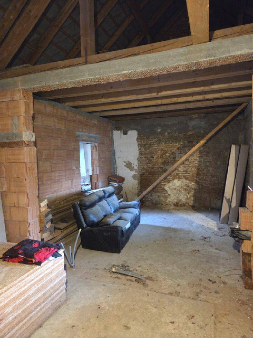 Unfertiger Dachbodenraum mit freiliegenden Ziegelwänden, Holzbalken und einem alten Sofa.