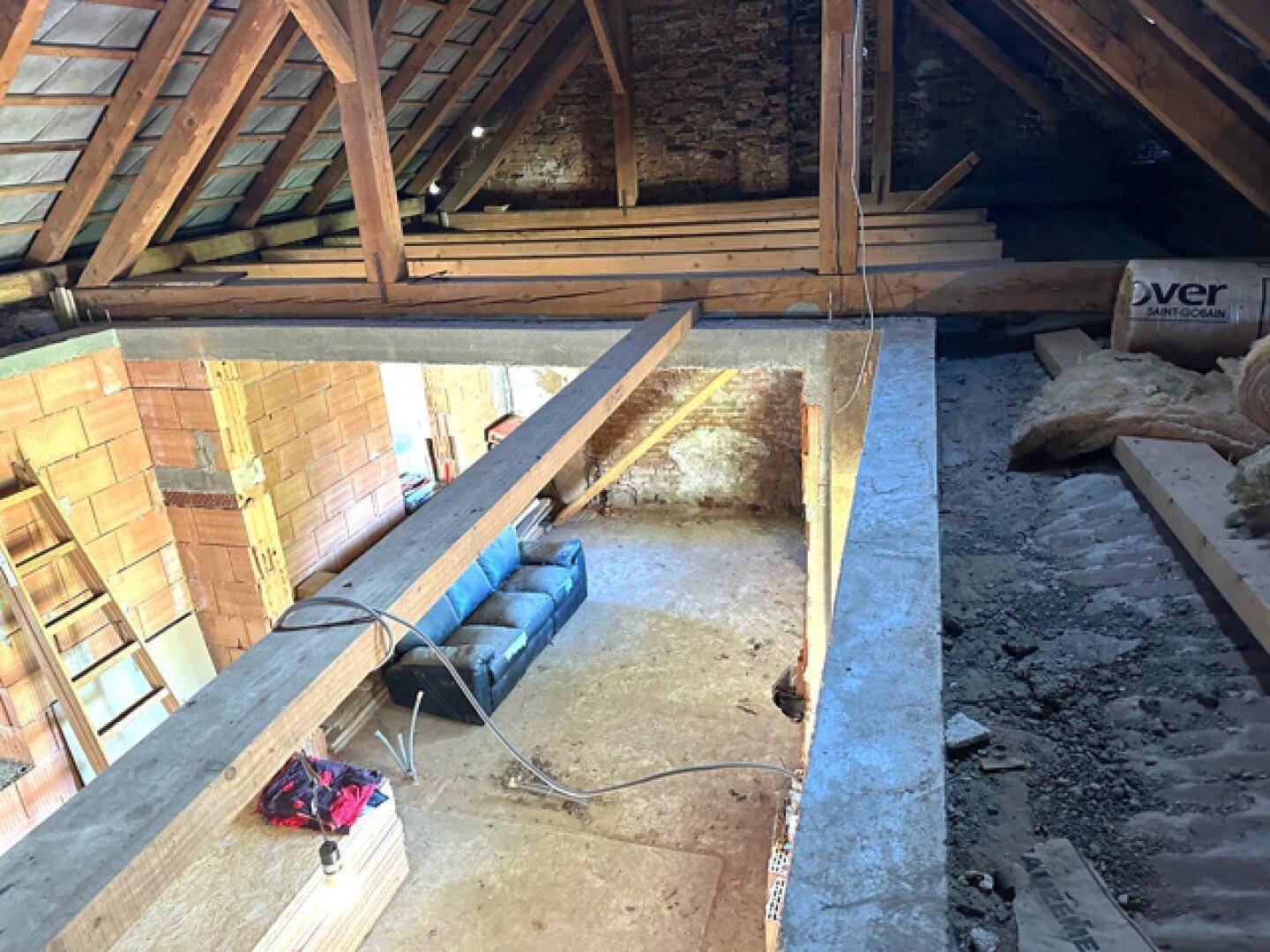 Blick von oben auf den unfertigen Dachboden mit sichtbaren Holzbalken und Ziegelwänden.