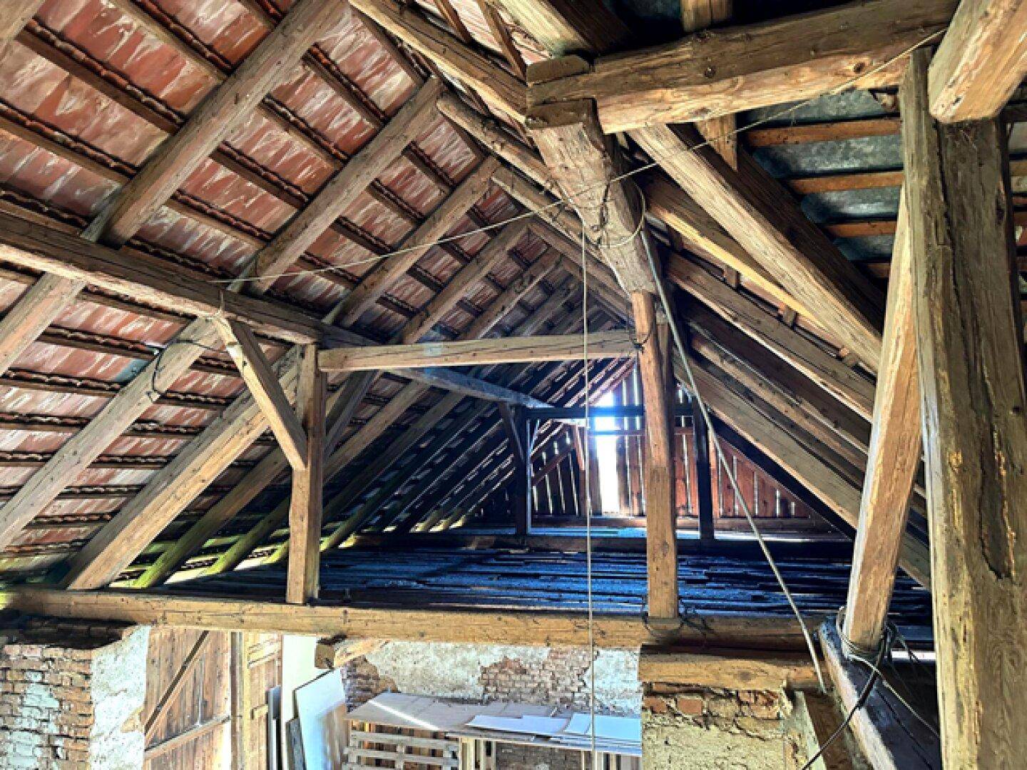 Innenansicht des Dachbodens mit sichtbaren Holzbalken und traditionellen Terrakotta-Dachziegeln.