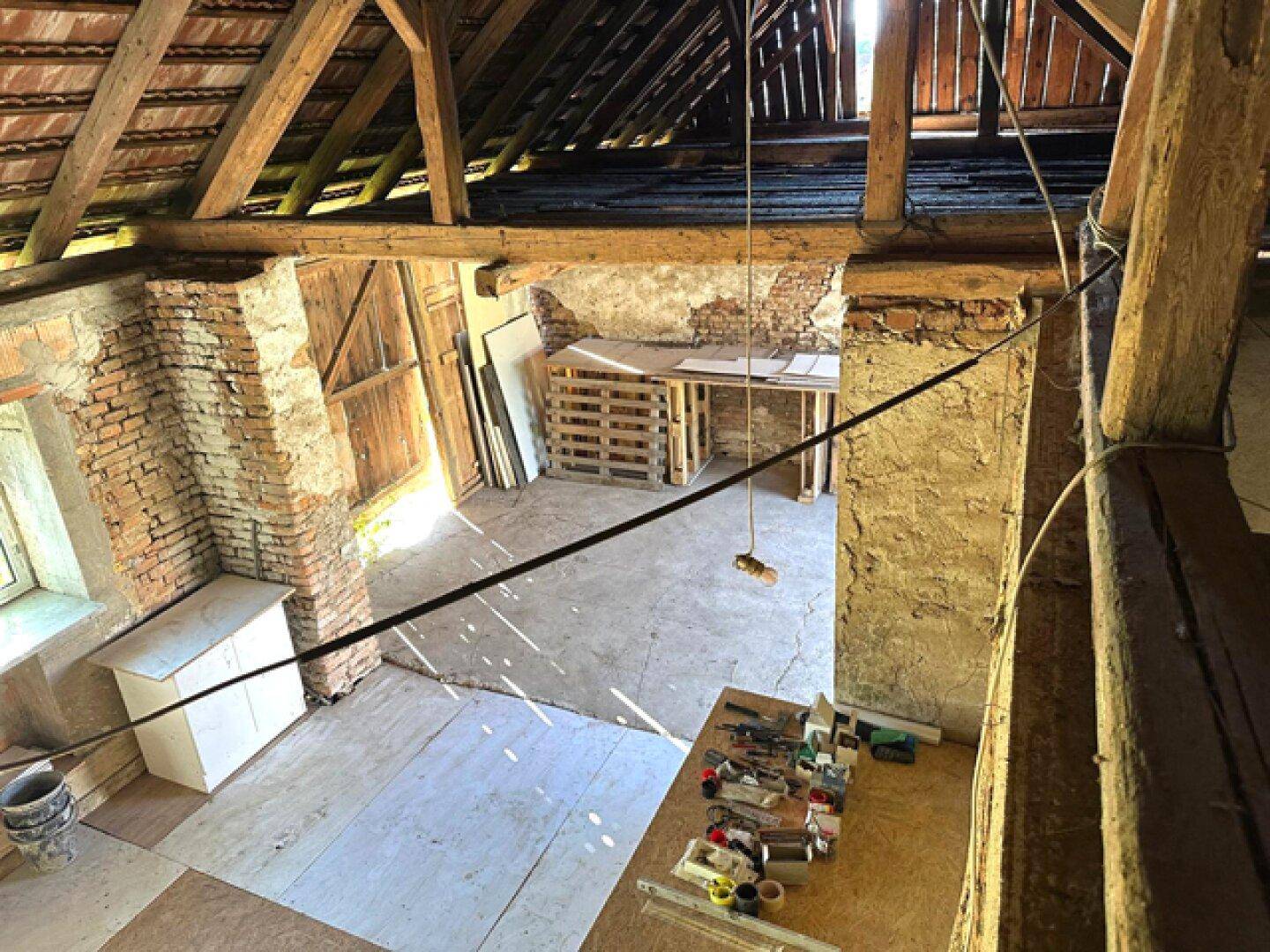 Weitläufiger Dachbodenbereich mit sichtbaren Holzbalken, Ziegelwänden und Baumaterialien.