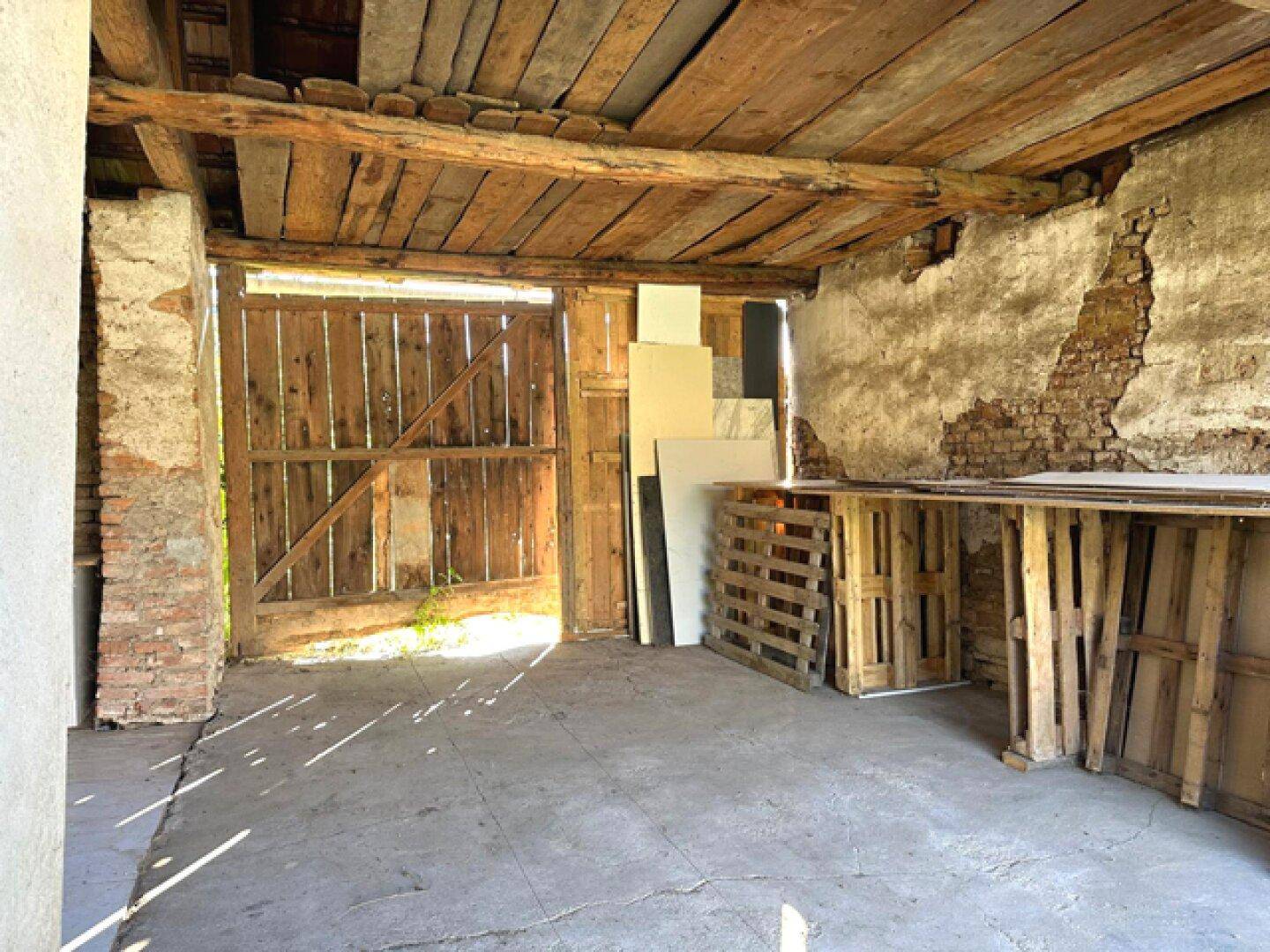 Großer, unfertiger Raum im Erdgeschoss mit Holztoren, Ziegelwänden und Betonboden.