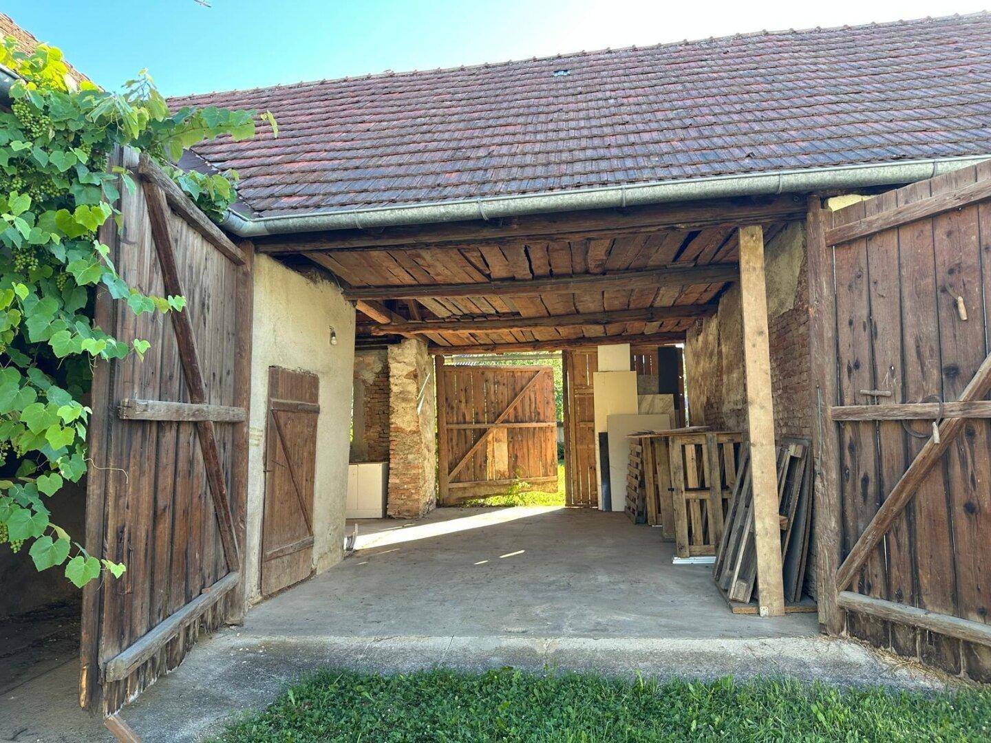 Außenansicht eines Gebäudes mit großen Holztoren, sichtbarem Dach und umgebendem Grün.