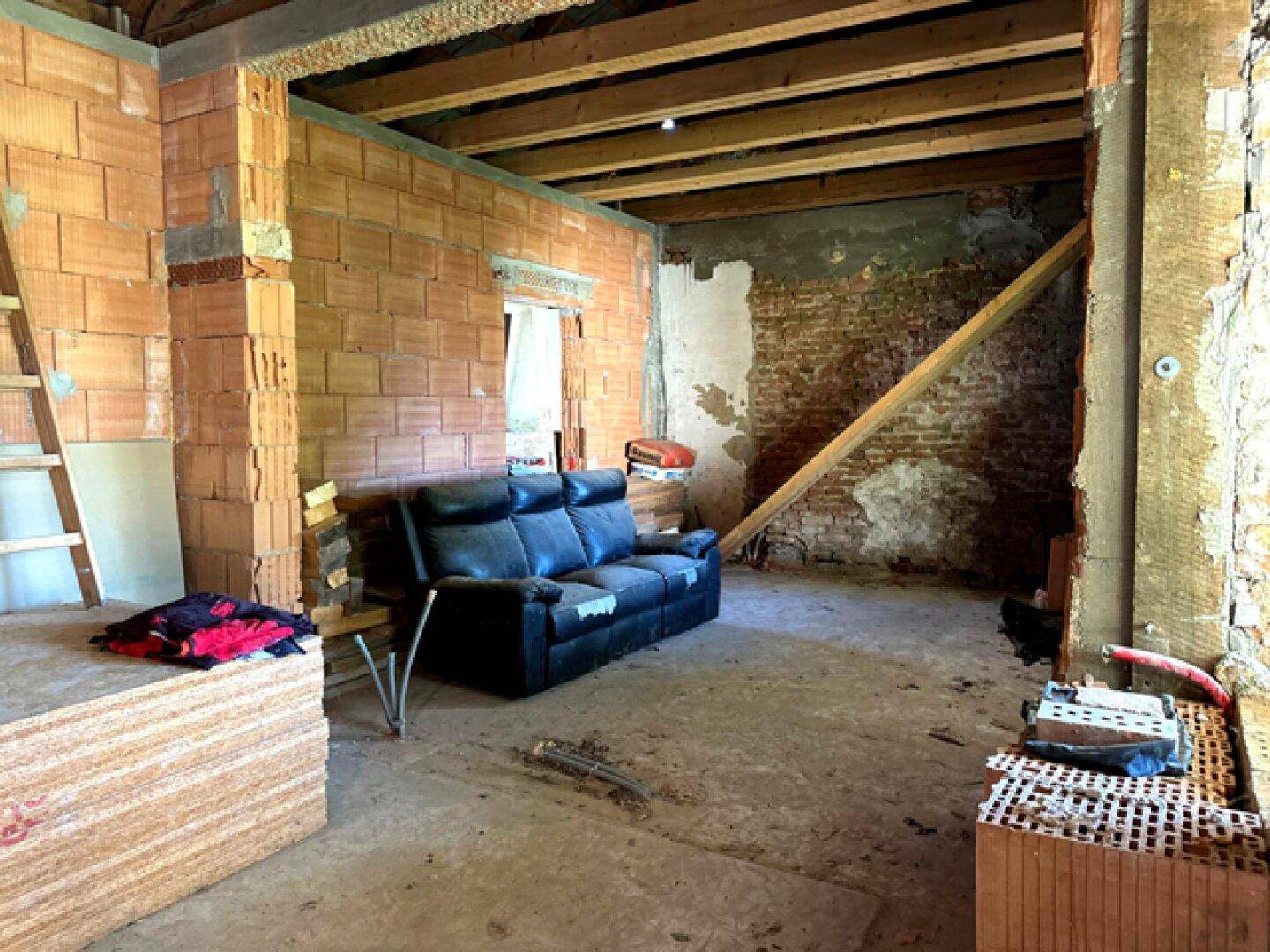 Rohbau-Wohnzimmer mit freiliegenden Ziegelwänden und Holzbalken, bereit für den Ausbau.