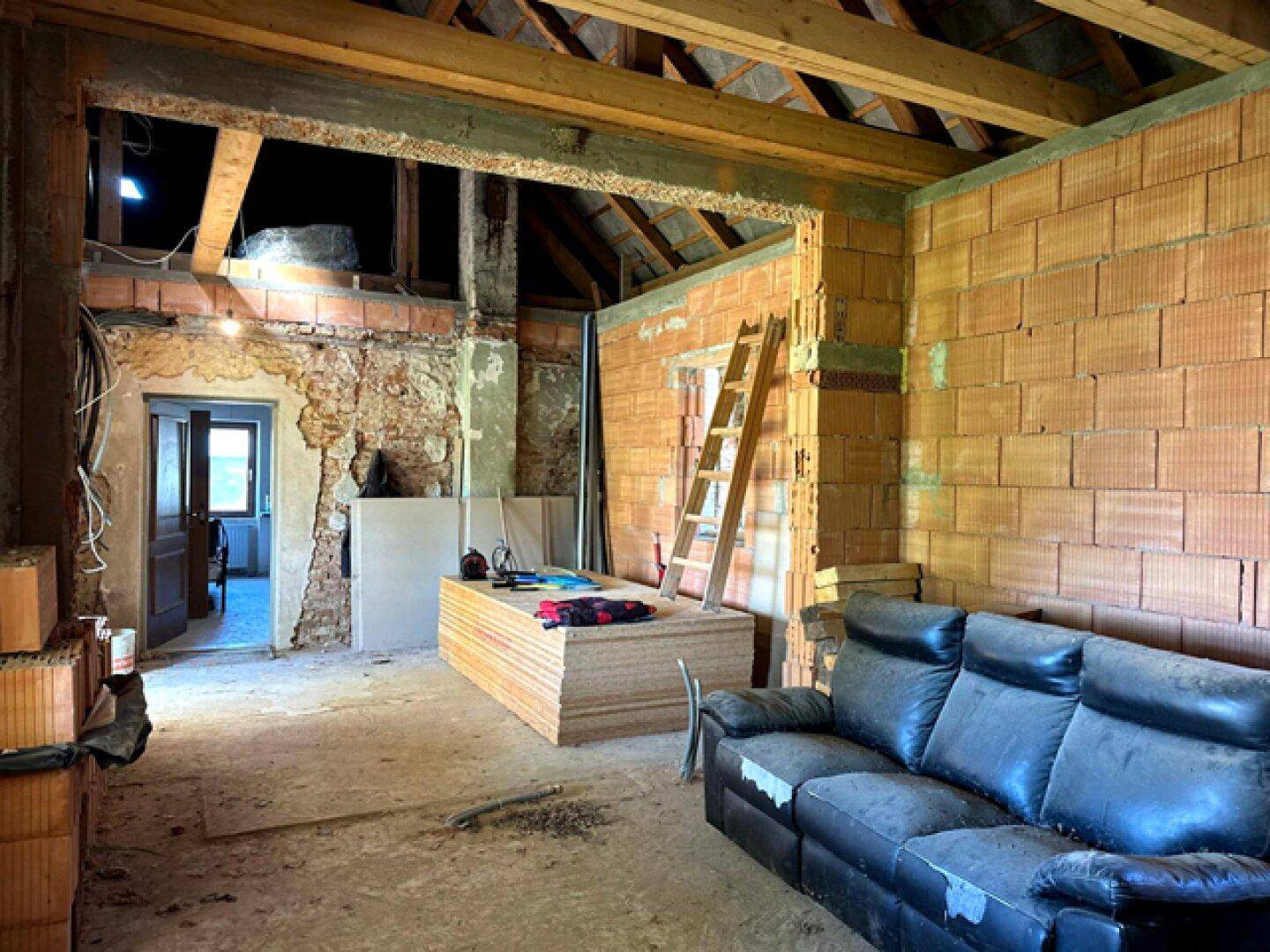 Geräumiger Wohnbereich im Rohbau mit freiliegenden Ziegelwänden und Holzbalkendecke.