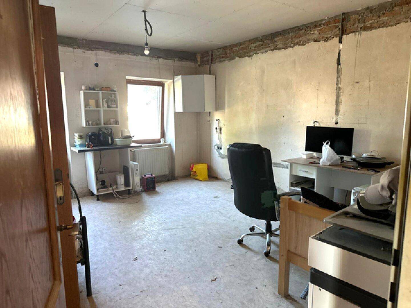Einfaches Arbeitszimmer mit Schreibtisch, Stuhl und provisorischer Küchenzeile.