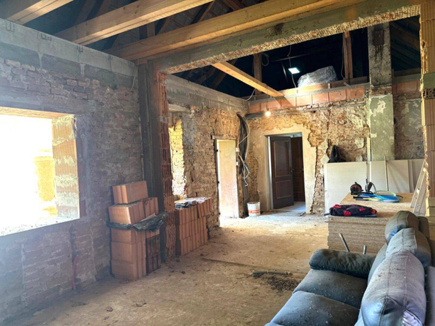 Großer Raum im Rohbau mit freiliegenden Ziegelwänden und sichtbaren Holzbalken.