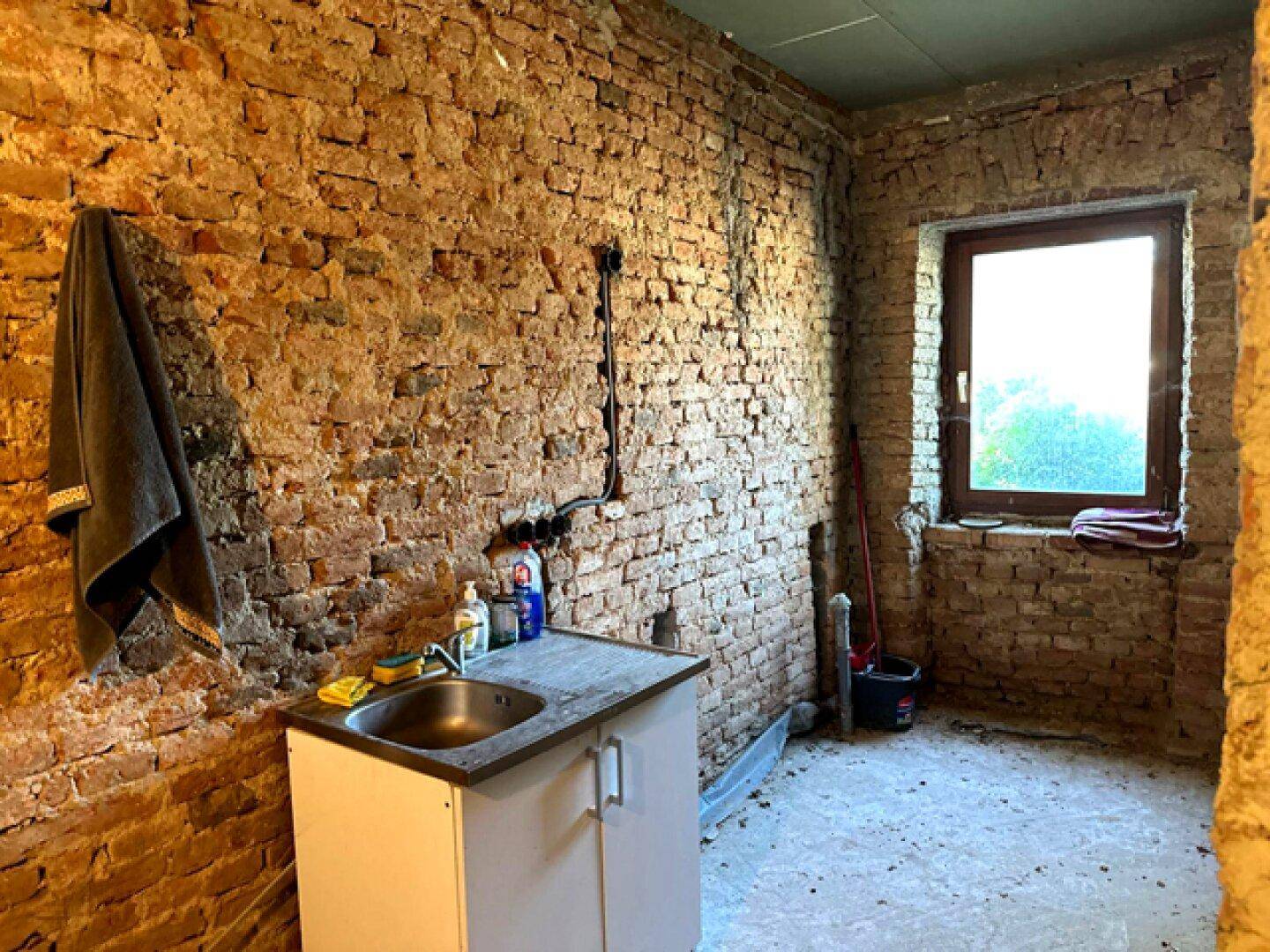 Einfacher Hauswirtschaftsraum mit freiliegenden Ziegelwänden und kleinem Waschbecken.