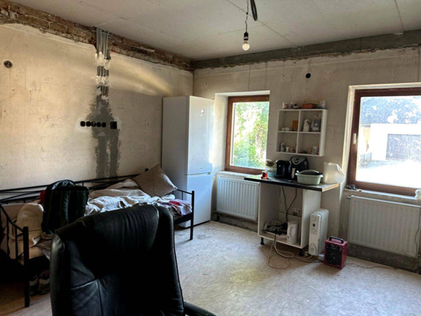 Schlafzimmer mit Bett, Schreibtisch und Kühlschrank, das auf Fertigstellung wartet.