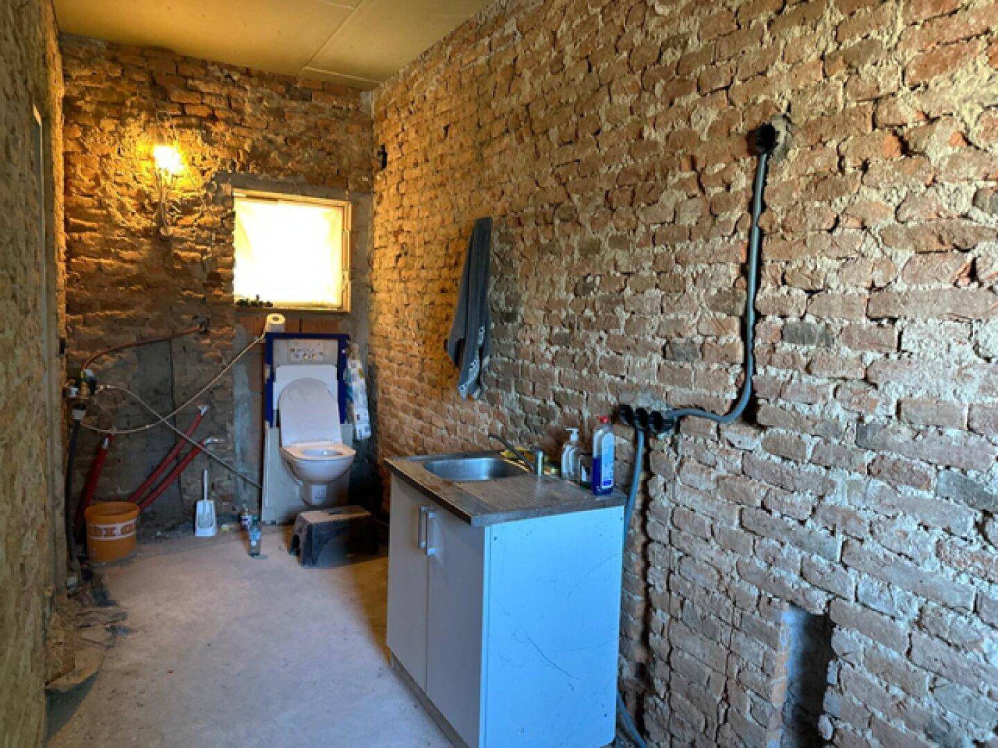 WC-Raum im Rohbau mit freiliegenden Ziegelwänden, Toilette und Waschbecken.