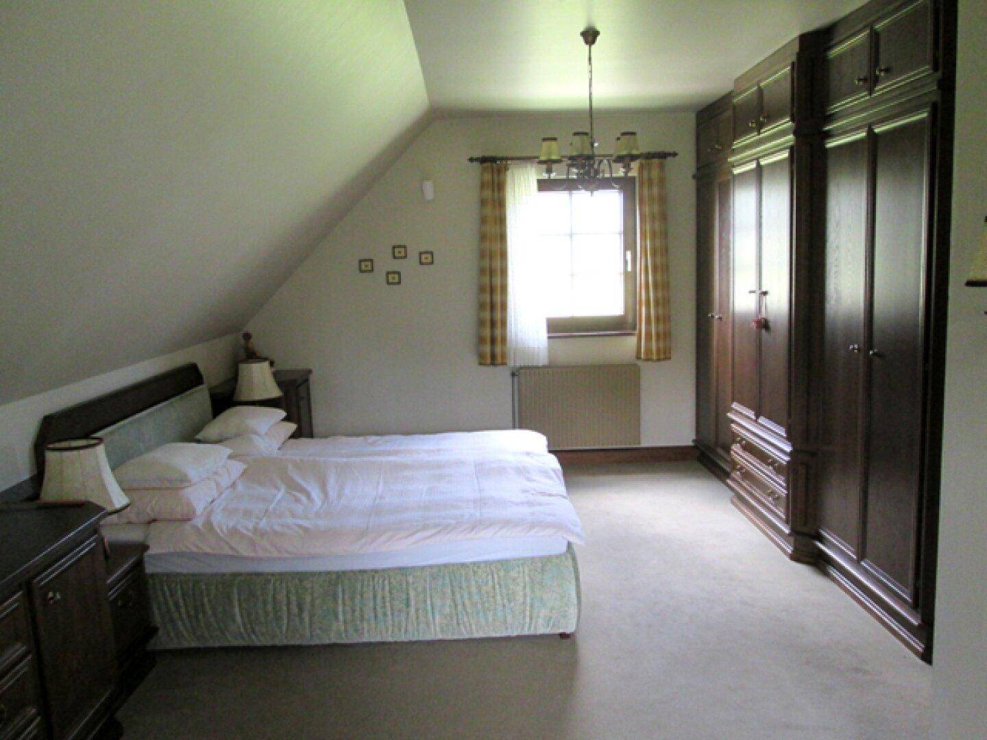 Schlafzimmer mit großem Holzschrank, Doppelbett und Fenster im Dachgeschoss.