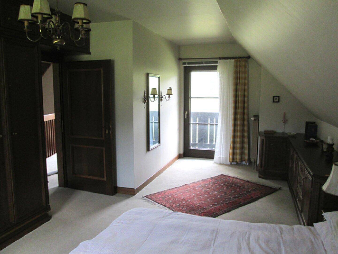 Schlafzimmer mit Zugang zum Balkon, Teppichboden und traditionellen Möbeln.