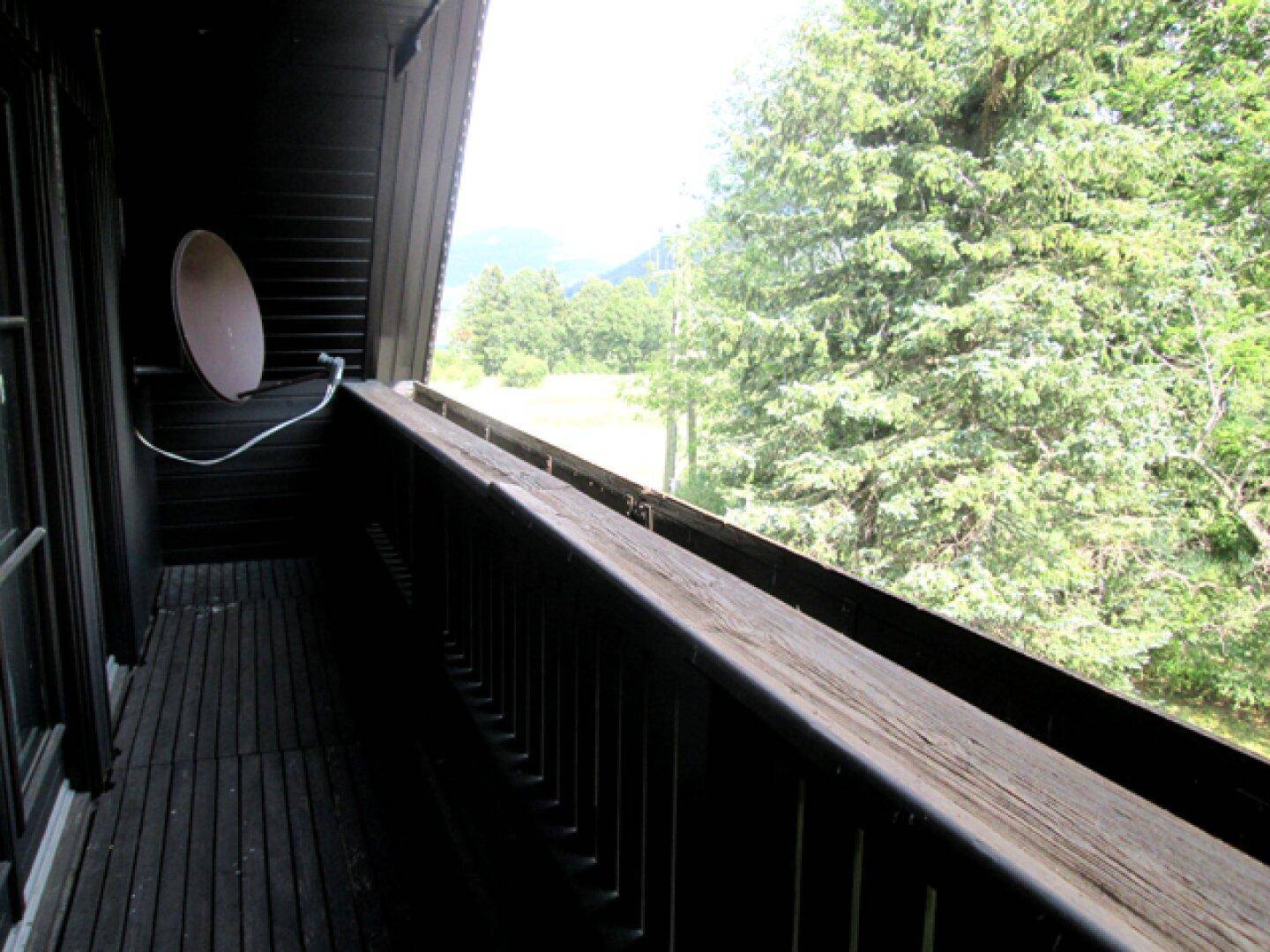 Holzbalkon mit Satellitenschüssel und weitem Blick in die Natur.