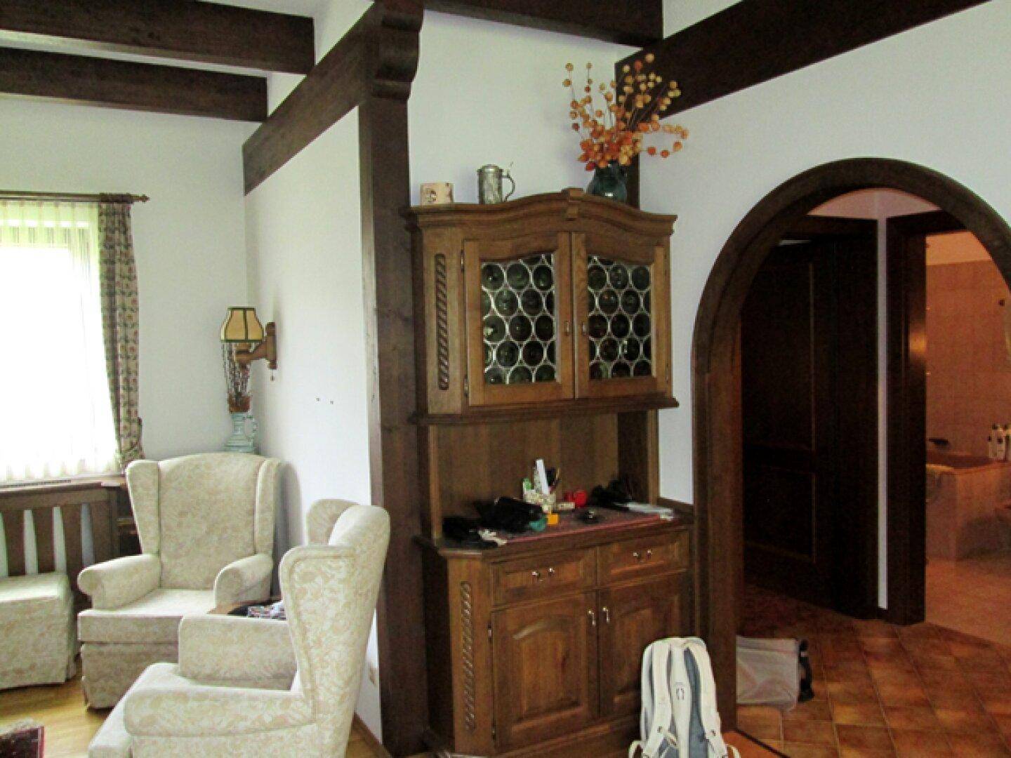 Wohnbereich mit Holzbalken, traditionellem Schrank und Durchgang zu einem weiteren Raum.