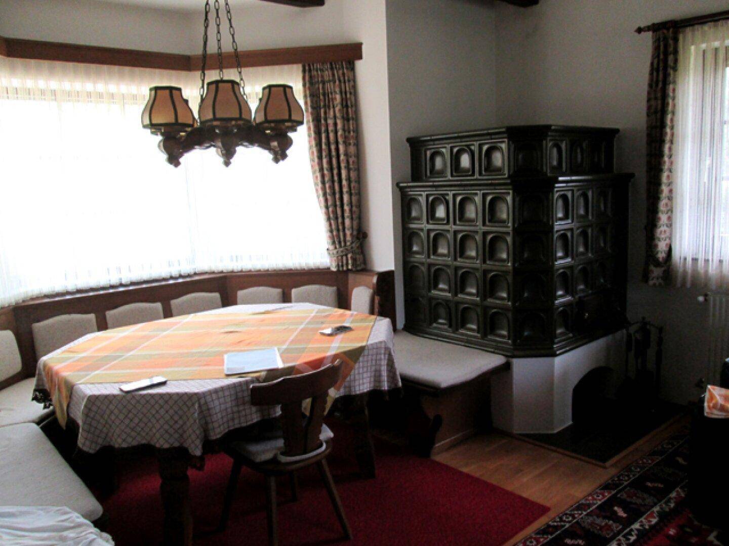 Heller Essbereich mit traditionellem Kachelofen, Holztisch und Eckbank am Fenster.