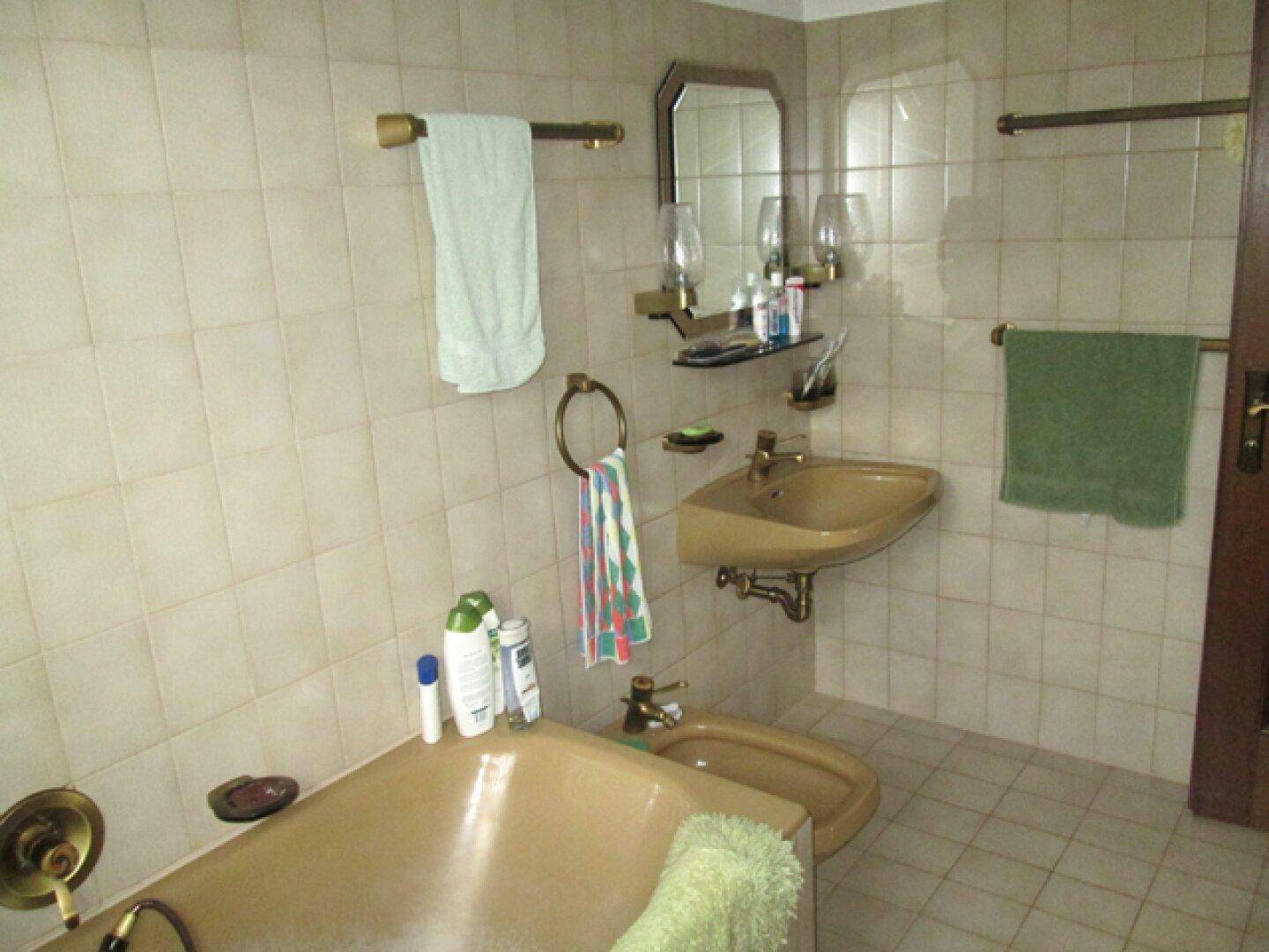 Badezimmer mit beigefarbenen Fliesen, Badewanne, Bidet und Spiegelschrank.