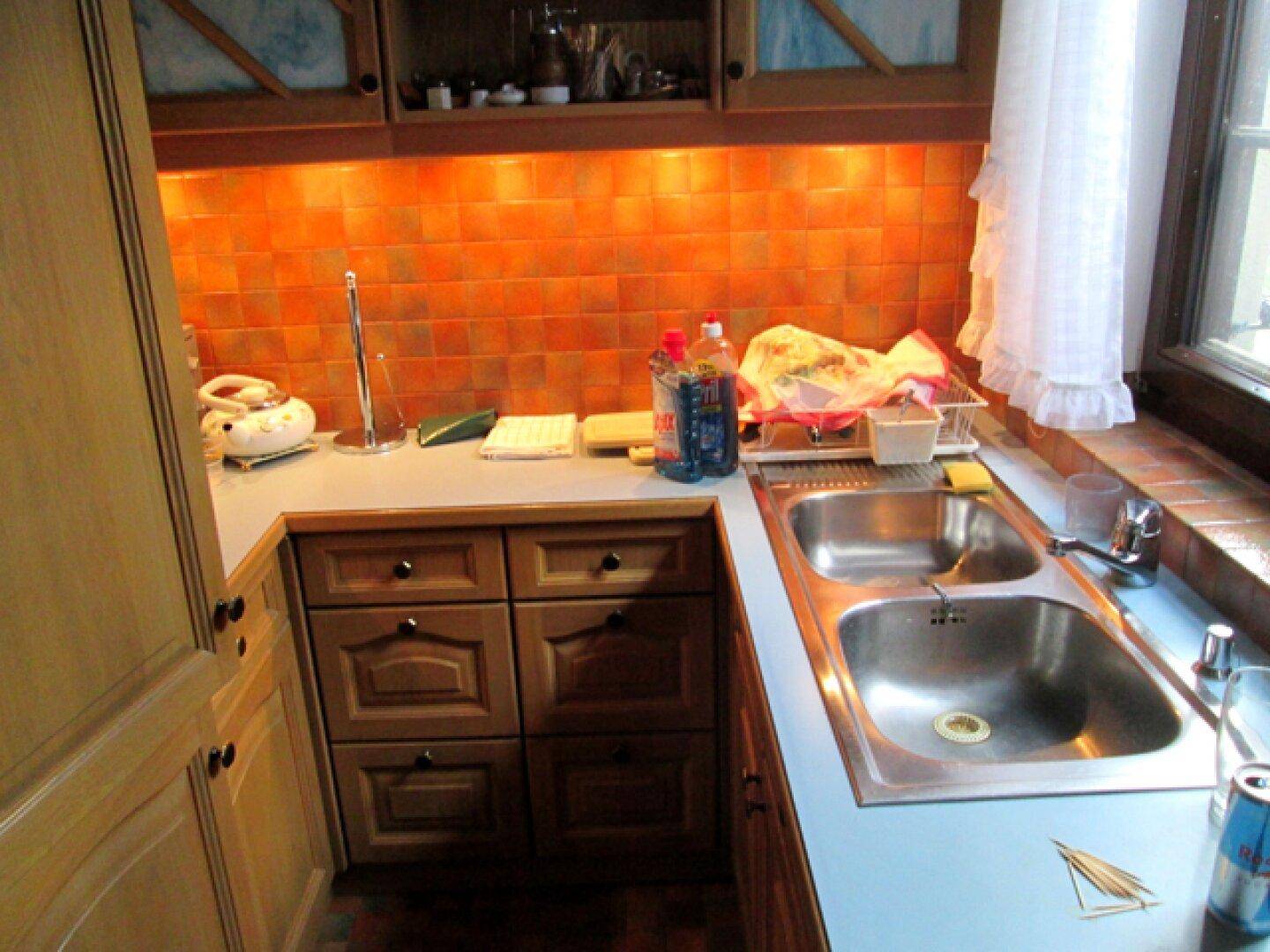 Kleine Küche mit Holzschränken, Doppelspüle und orangefarbenen Fliesen als Spritzschutz.