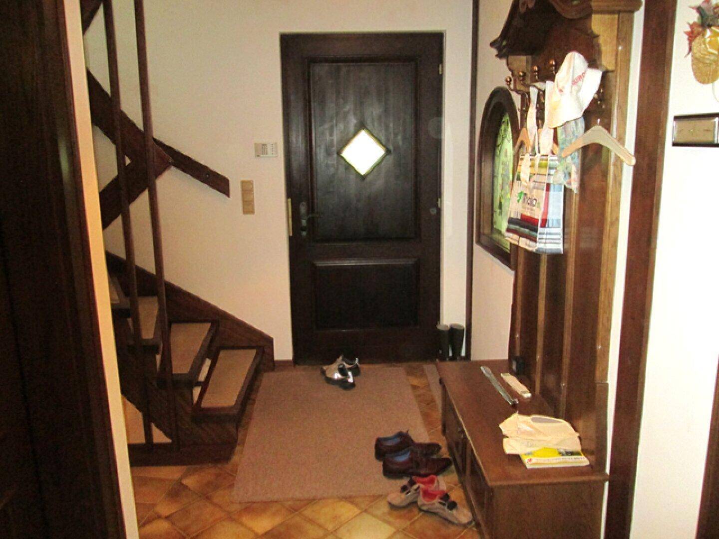 Eingangsbereich mit Holztreppe, Garderobe und gefliestem Boden.