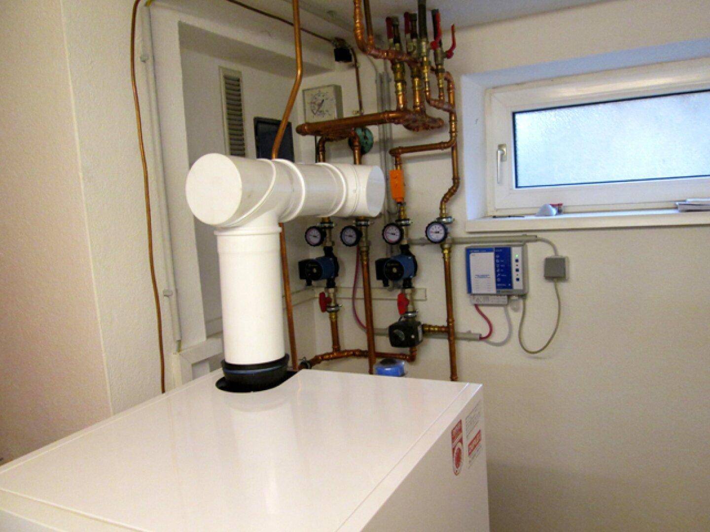 Heizungsraum mit sichtbaren Kupferrohren, Ventilen und einem Fenster für Belüftung.