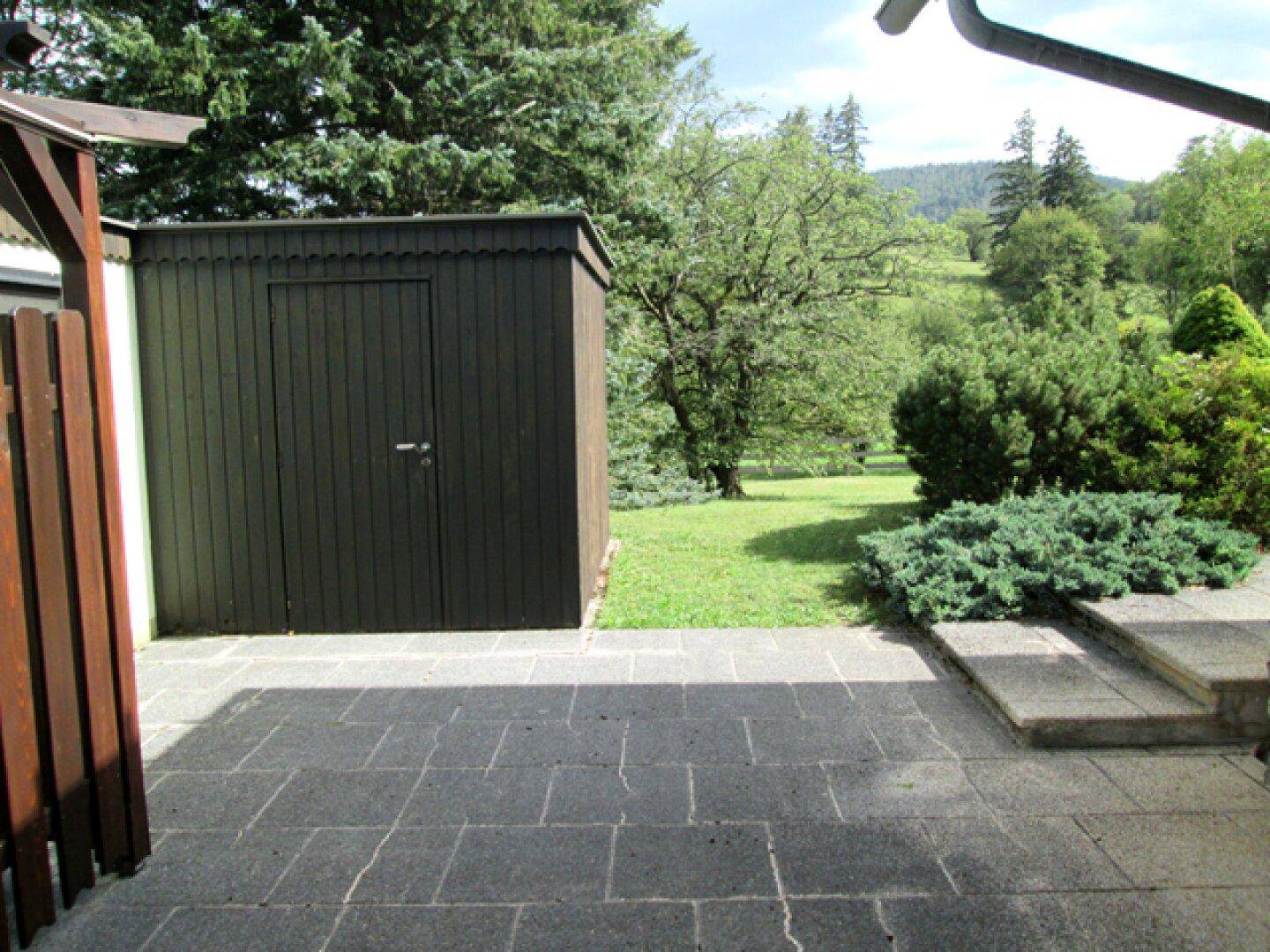 Terrasse neben einem Holzschuppen mit Blick auf den weitläufigen grünen Garten.