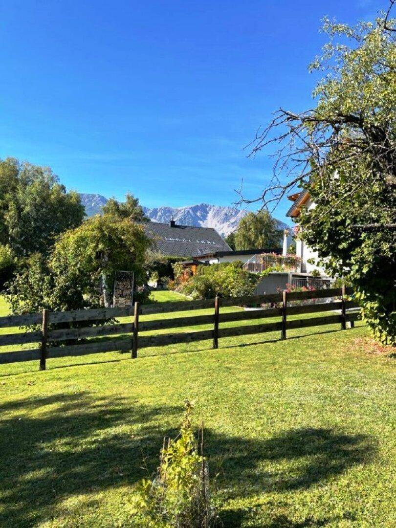 Weitläufiger Gartenbereich mit Holzzaun und Blick auf die Berge im Hintergrund.