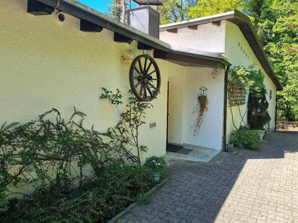 Eingangsbereich eines weißen Hauses mit gepflastertem Weg, dekoriert mit einem alten Wagenrad und Pflanzen.