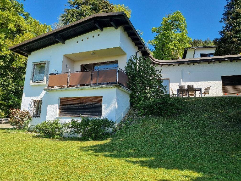 Weißes Wohnhaus mit Balkon und einer Terrasse im Erdgeschoss, umgeben von grüner Natur.