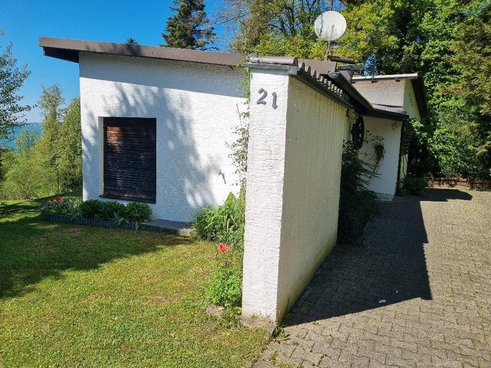 Kleines weißes Gebäude mit der Hausnummer 21, umgeben von einem gepflegten Rasen und einer Zufahrt.