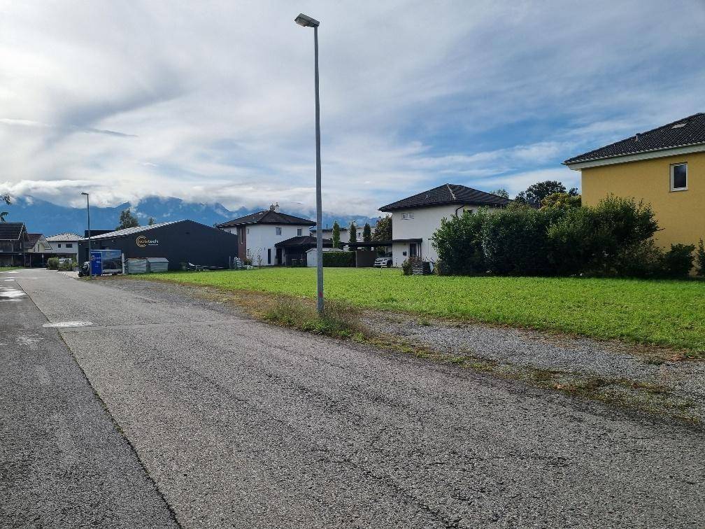 Weitläufige Grünfläche neben einer Straße mit Blick auf die umliegende Wohnbebauung und Berge.