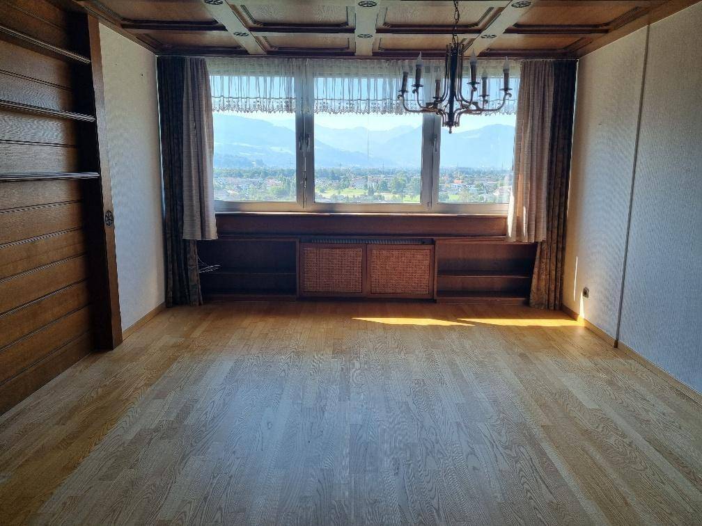 Geräumiges Wohnzimmer mit Parkettboden, Holzdecke und großem Fenster mit Bergblick.